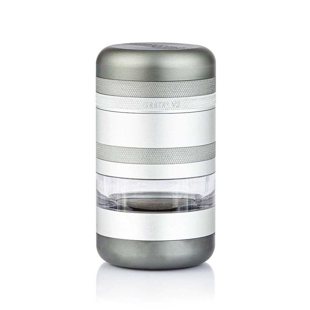 Front-facing studio shot of the RYOT GR8TR Jar Body Grinder showing its cylindrical silver and gray stacked sections with a clear middle chamber.