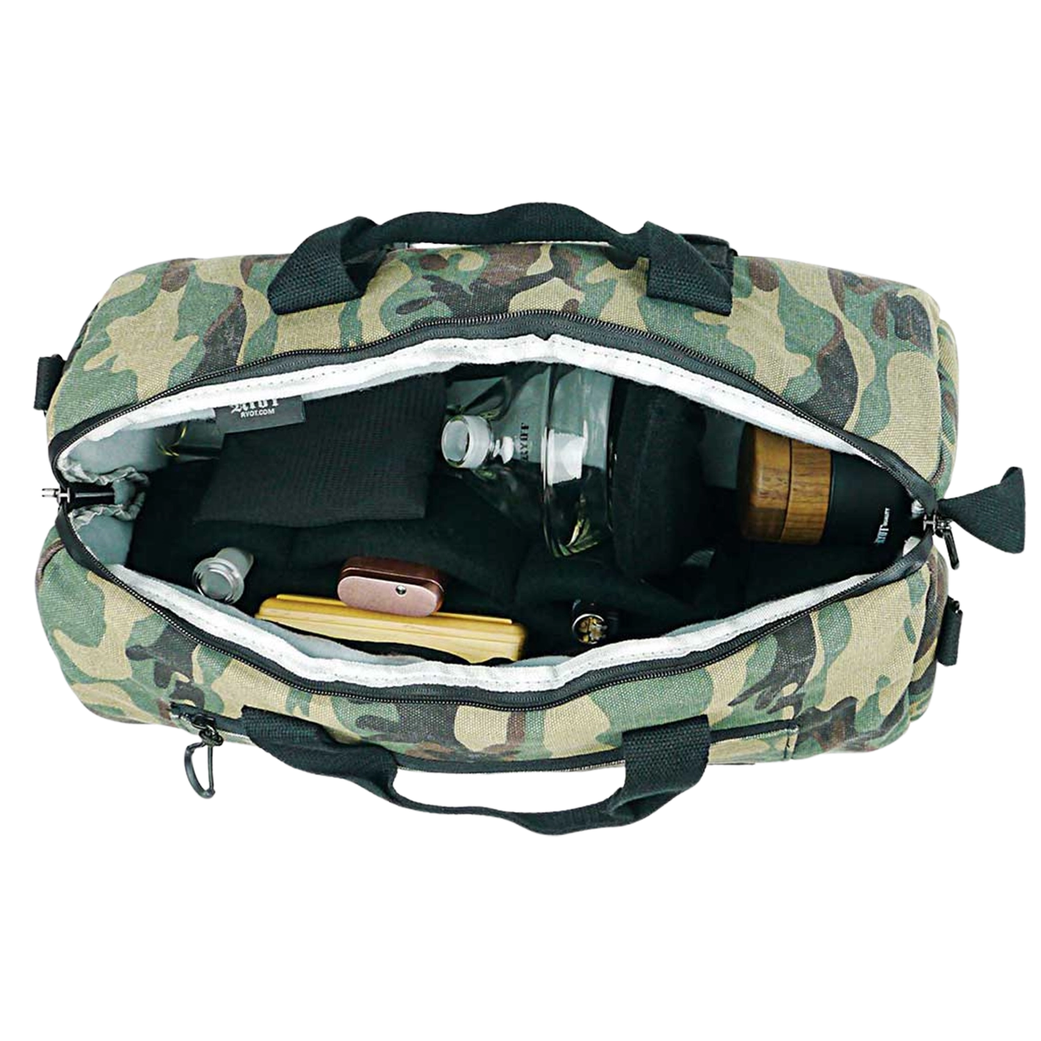 Top-down view into a camo RYOT Pro-Duffle Carbon Series Smell-Proof Bag with its zipper open showing padded black interior pockets and small glass and wooden items inside.