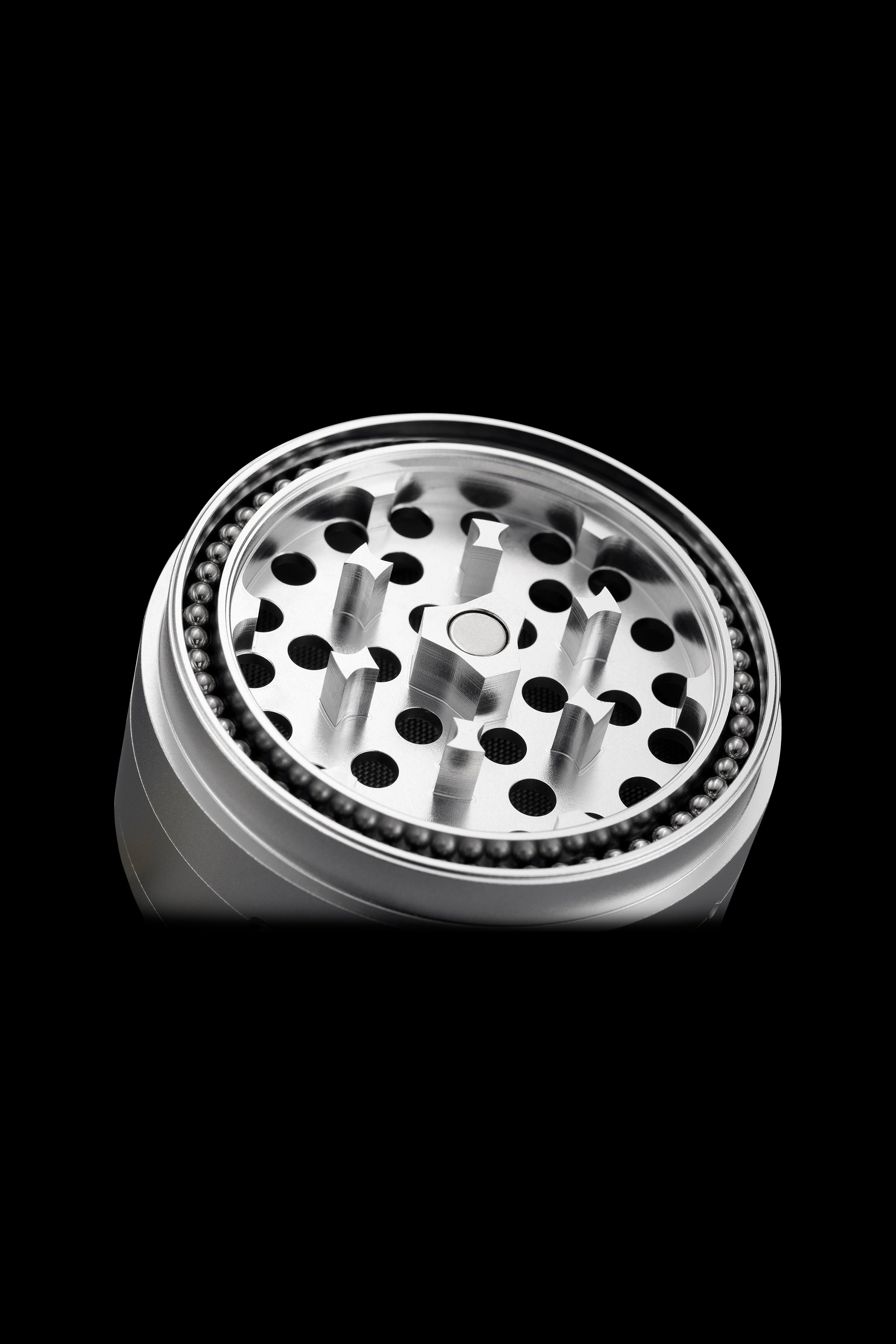 Silver cannabis grinder with visible grinding teeth and collection chamber, isolated on black.