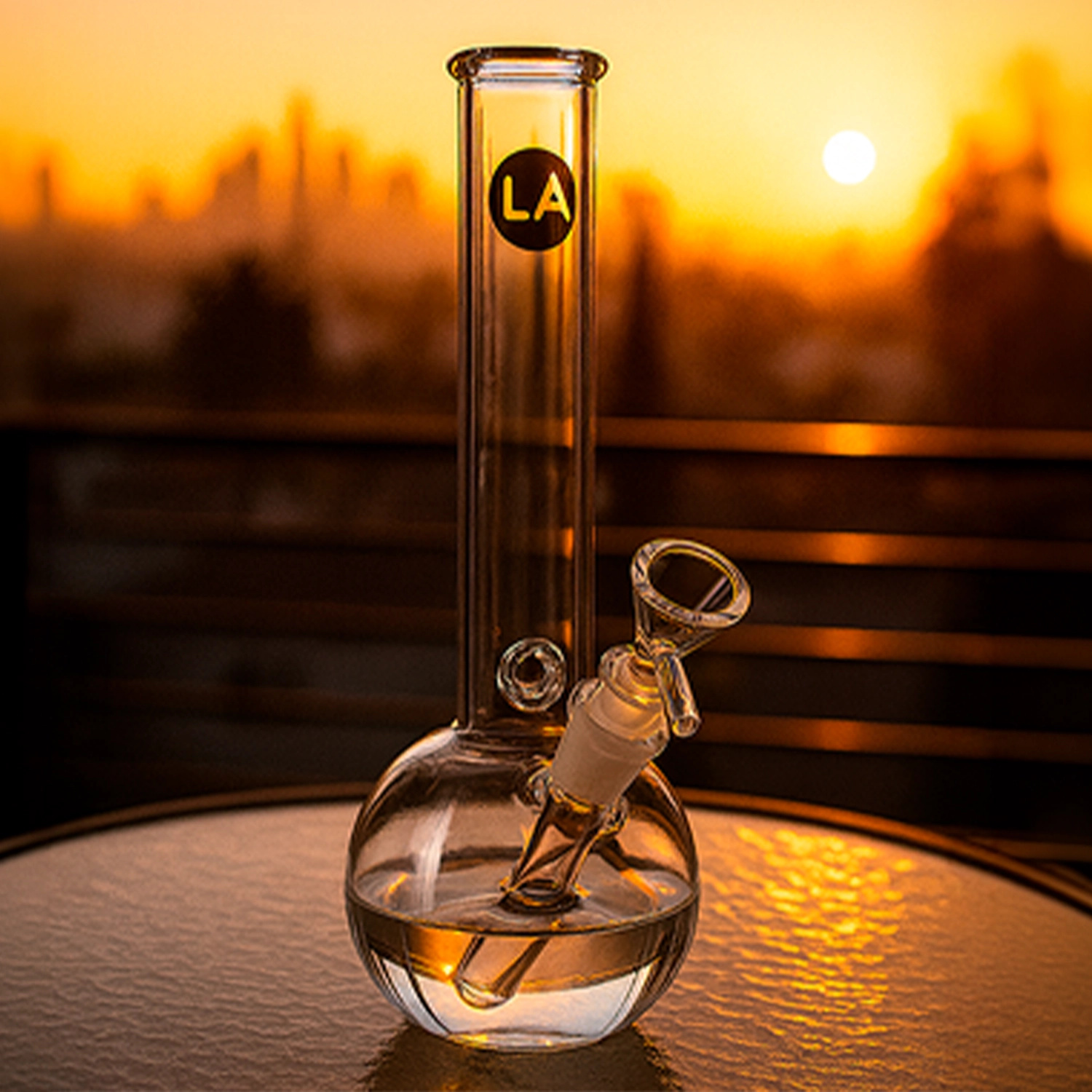 A front-facing shot of the LA Pipes "Baller" Bubble Base Bong glowing in sunset light, the clear glass sphere base and straight neck reflecting warm orange hues.