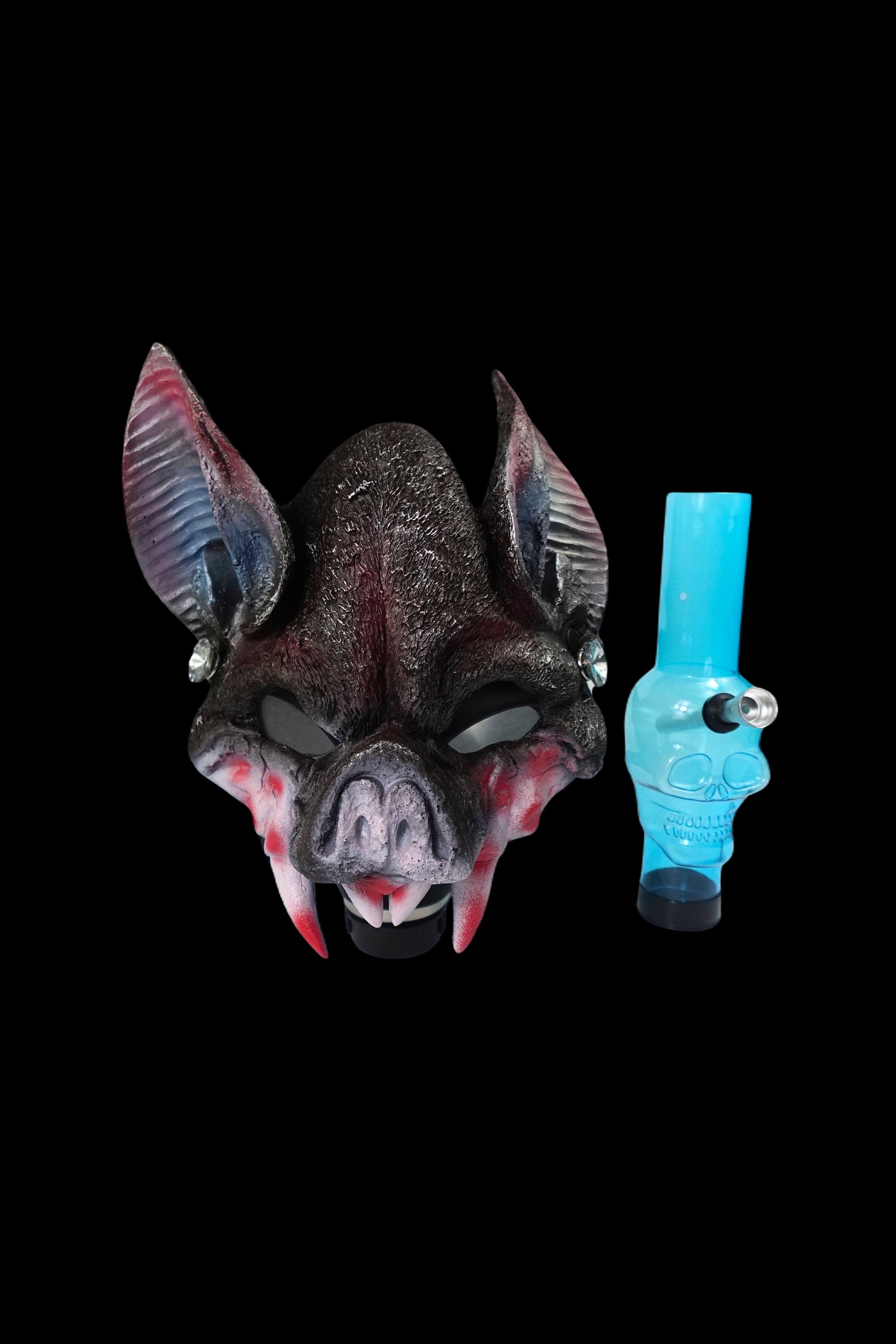 A spooky bat mask and blue glass pipe against a black background.