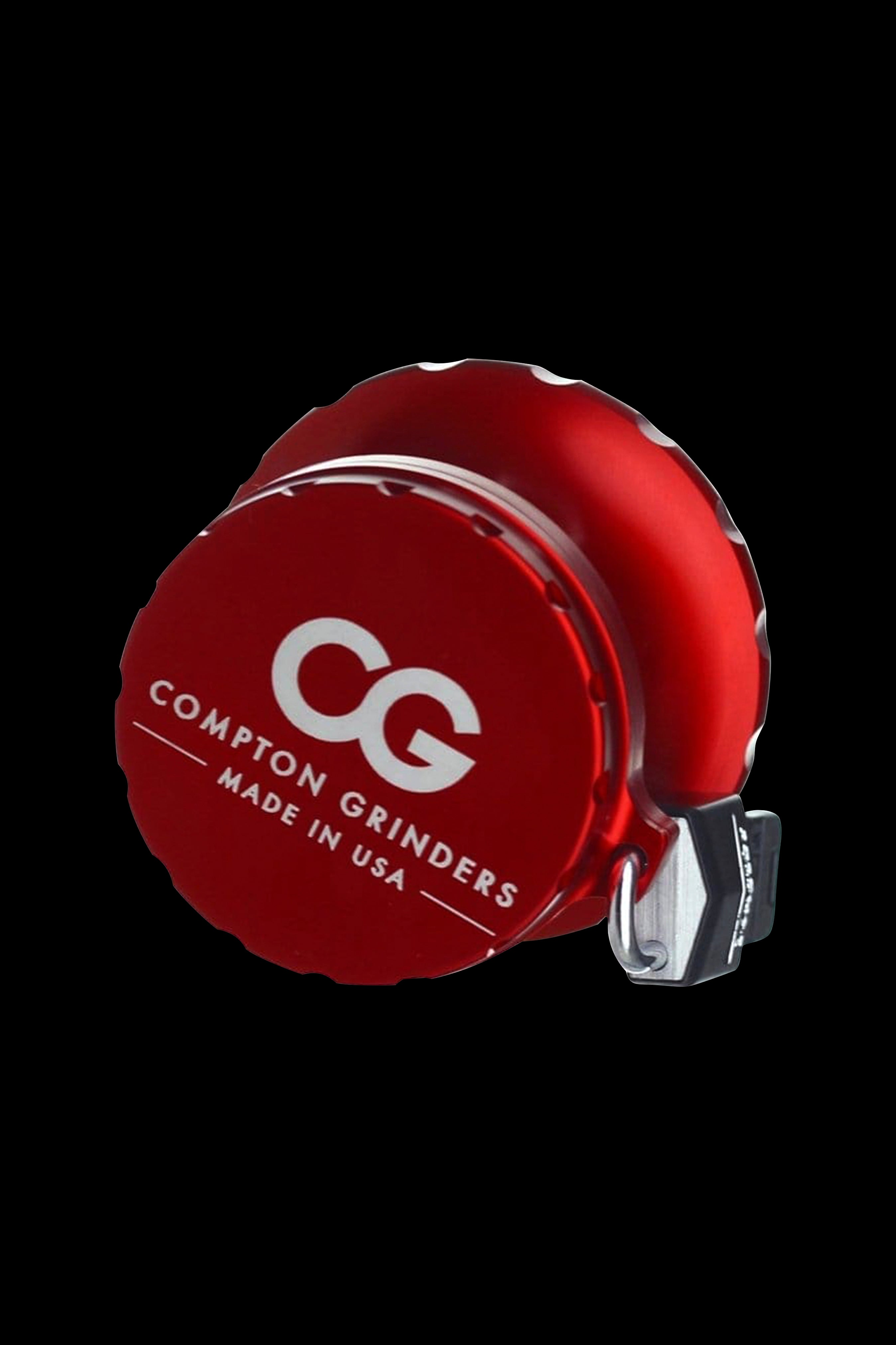 Red Compton Grinders cannabis grinder with white logo, isolated on black.