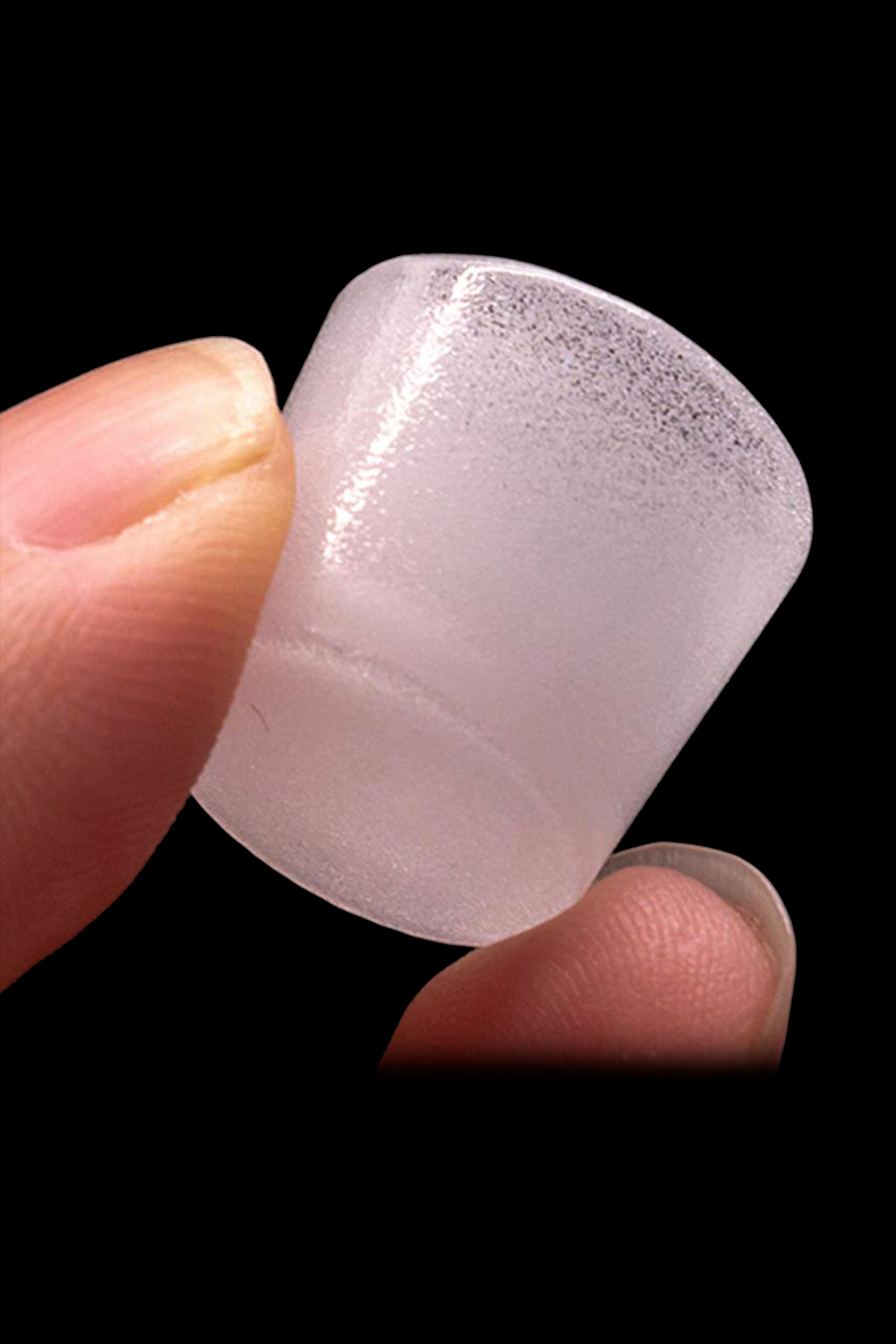 Close-up of a translucent, pink cannabis concentrate dab tool held between fingertips.