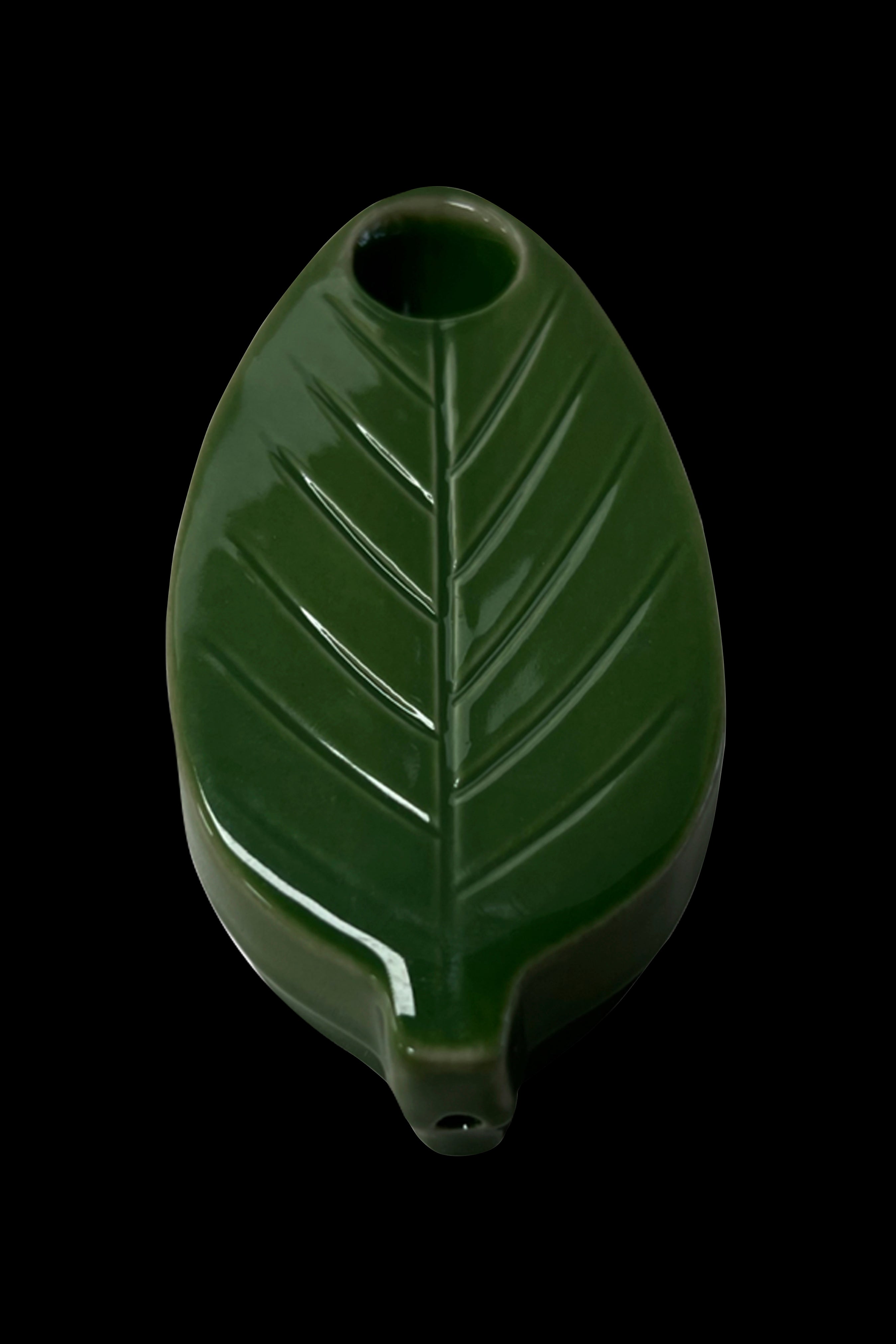 Green ceramic leaf-shaped pipe isolated on a black background.
