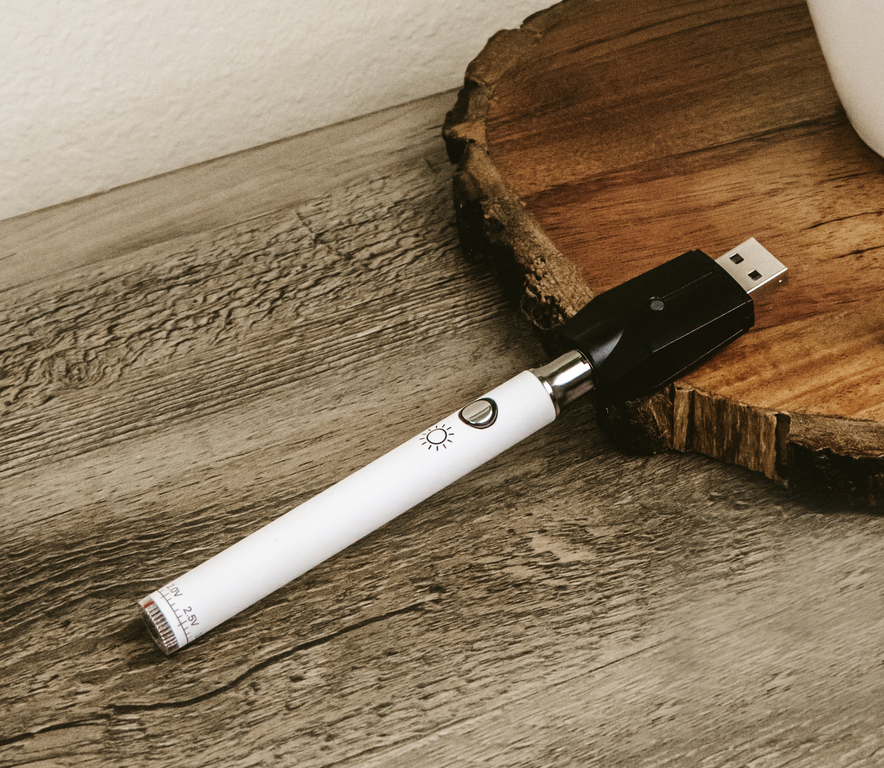 White cannabis vape pen with USB charging case on a wood surface.