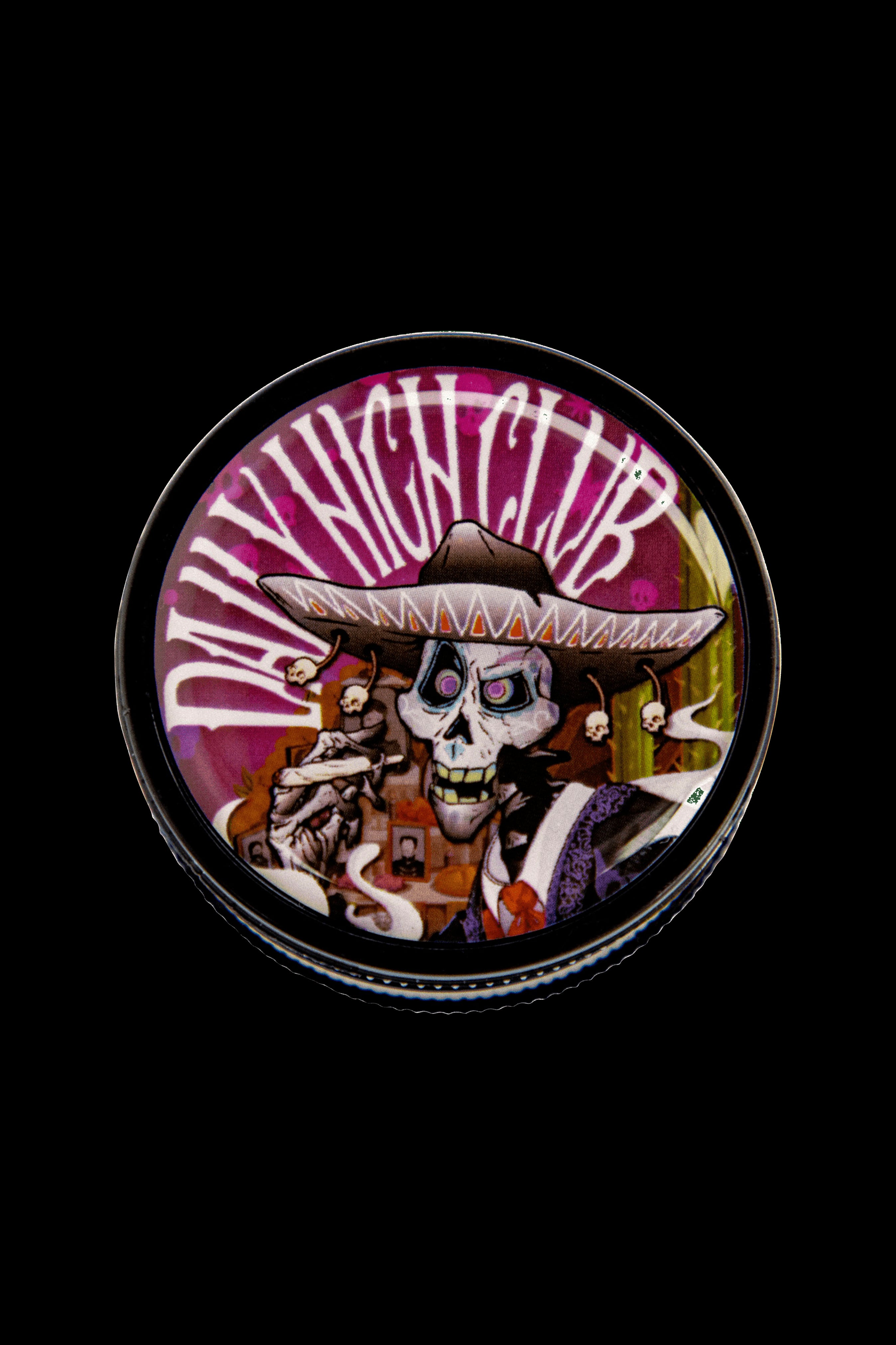 Close-up of a metal grinder with a Day of the Dead-style skull wearing a sombrero and the text “Day Nite Club” etched on the lid, set against a black background.