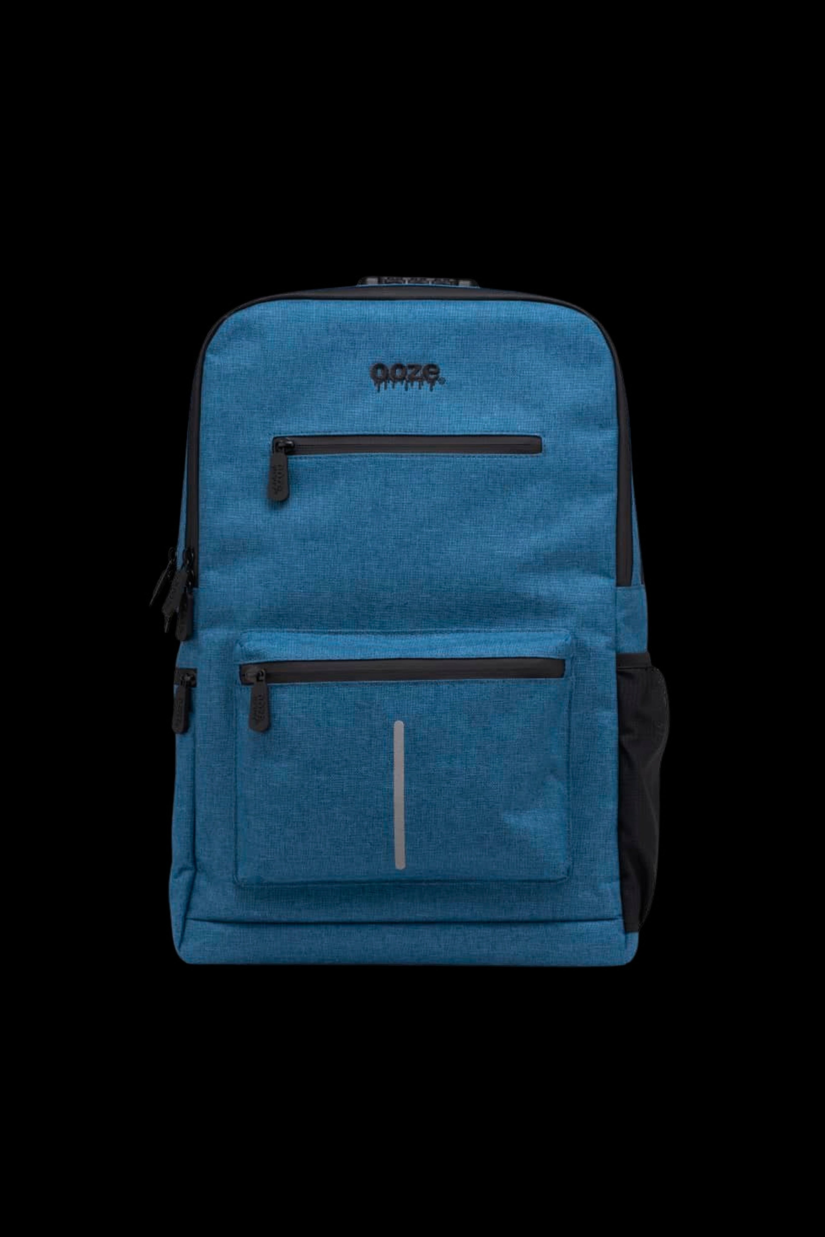 Front-facing crop of the blue Ooze Traveler Smell Proof Backpack showing its top pockets, logo, and vertical reflective strip against a black background