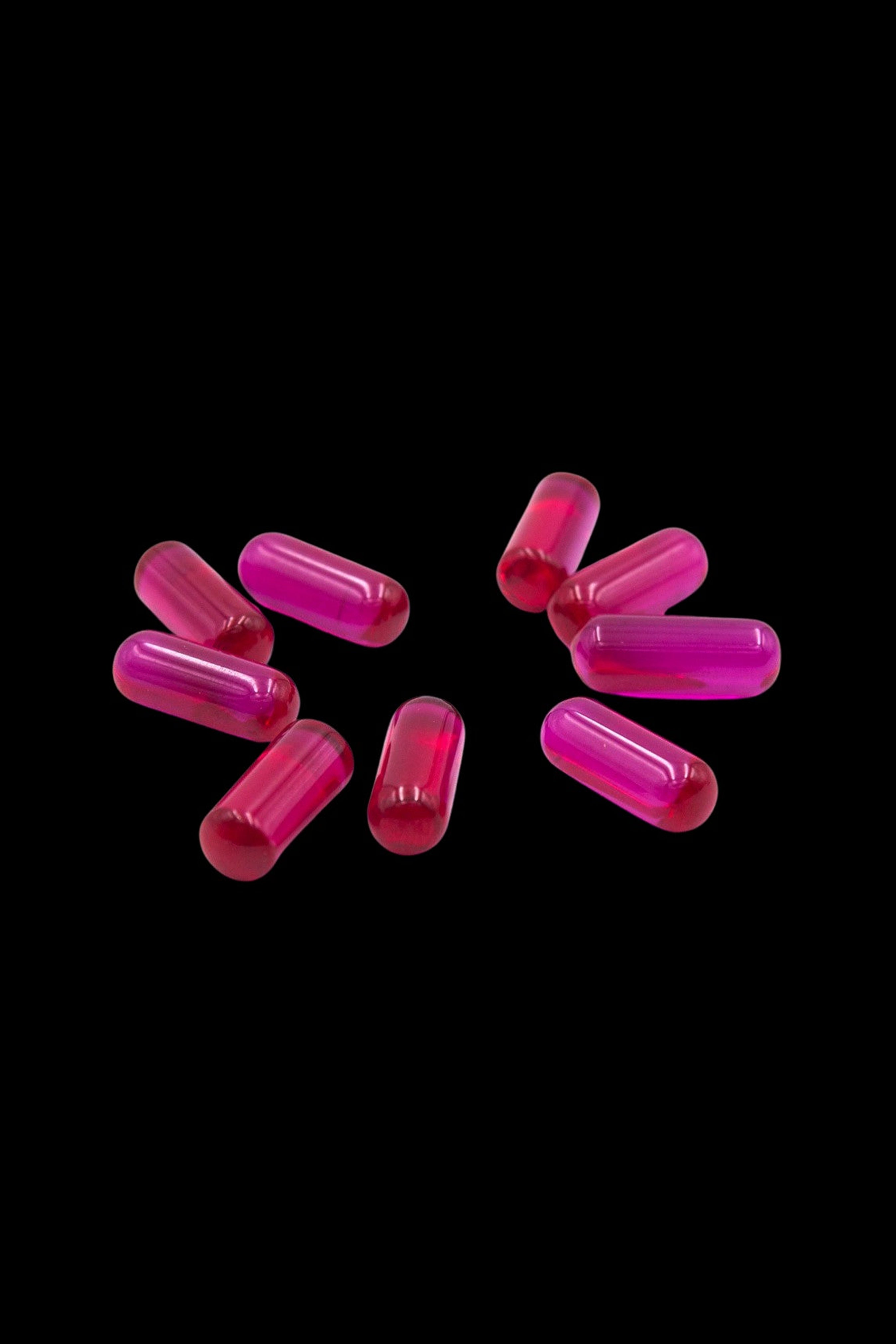 Pink cannabis capsules scattered on a black background.
