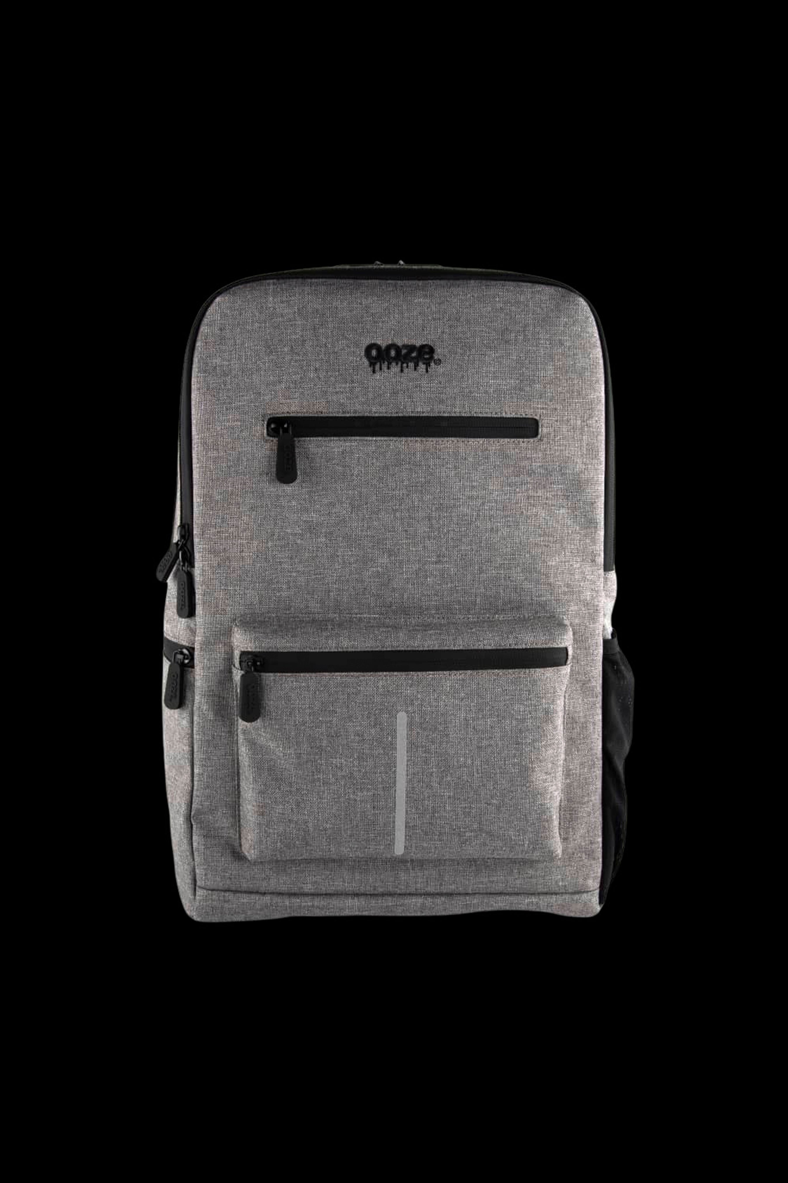 Centered front view of the gray Ooze Traveler Smell Proof Backpack showing its top logo, three zippered pockets, and vertical reflective strip.