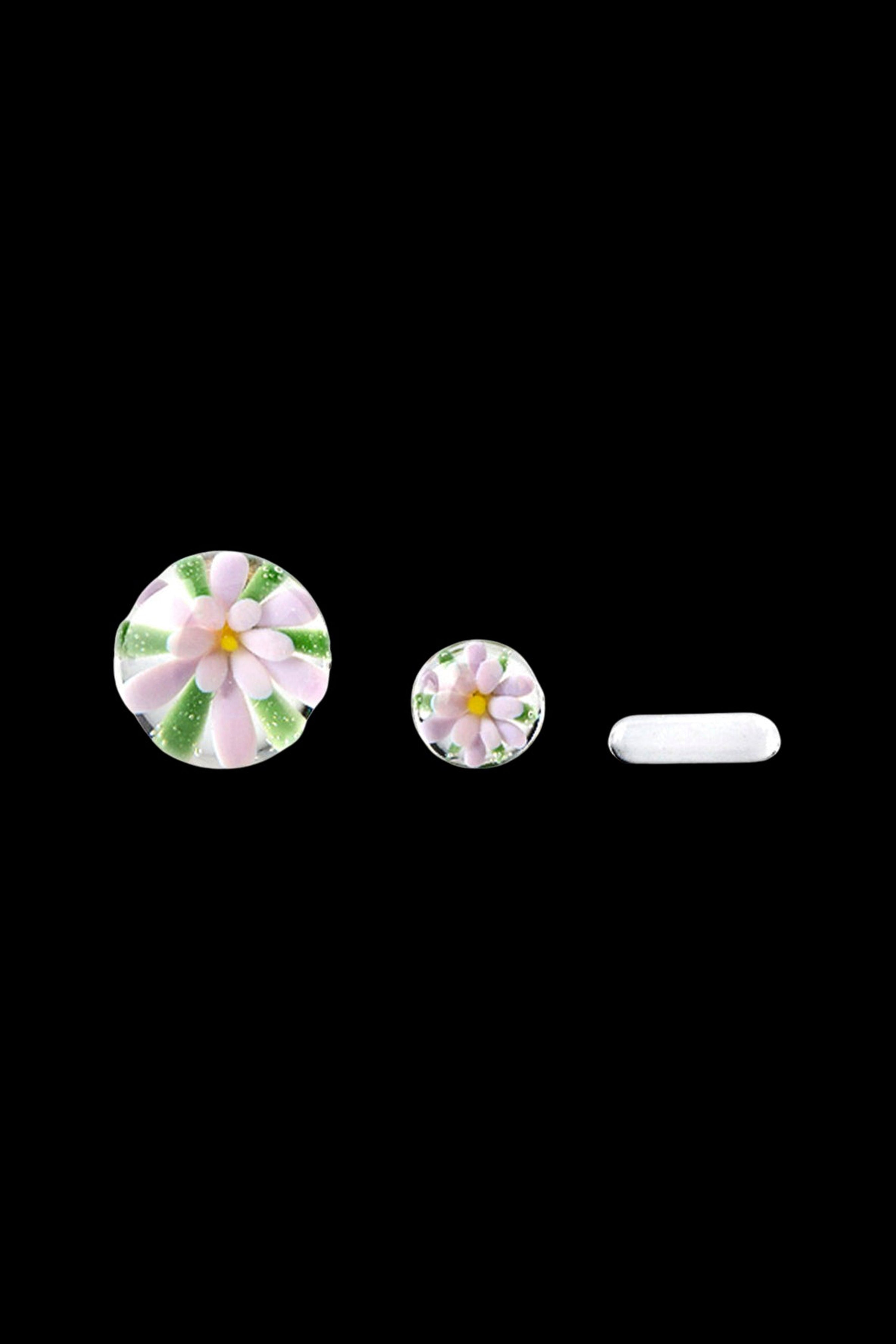 Hand-blown glass cannabis accessories featuring floral designs, including a cap, insert, and tip, against a black background.