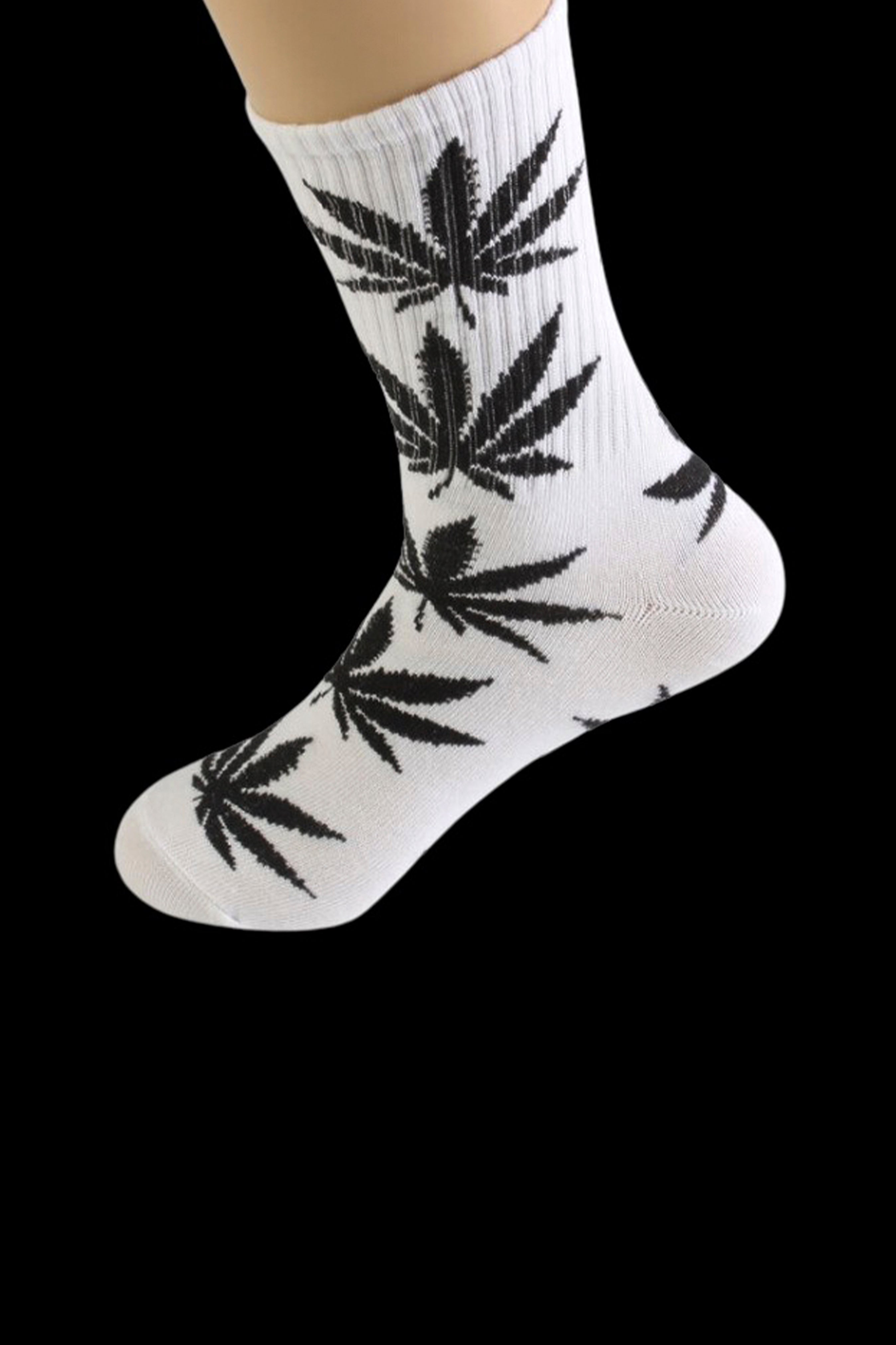 White crew socks with a repeating black cannabis leaf pattern, shown on a foot.