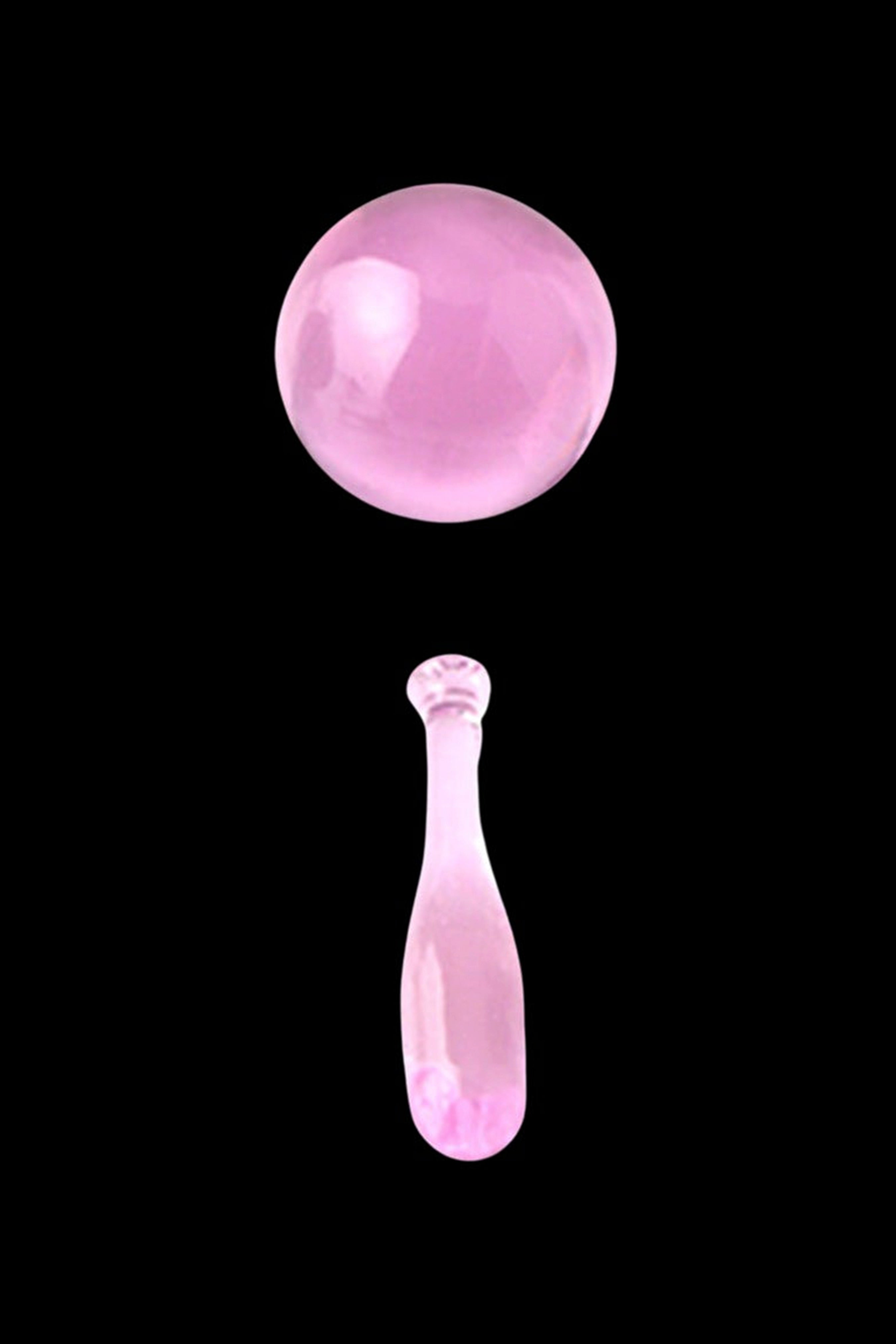 Pink glass cannabis oil droplet and sphere against a black background.