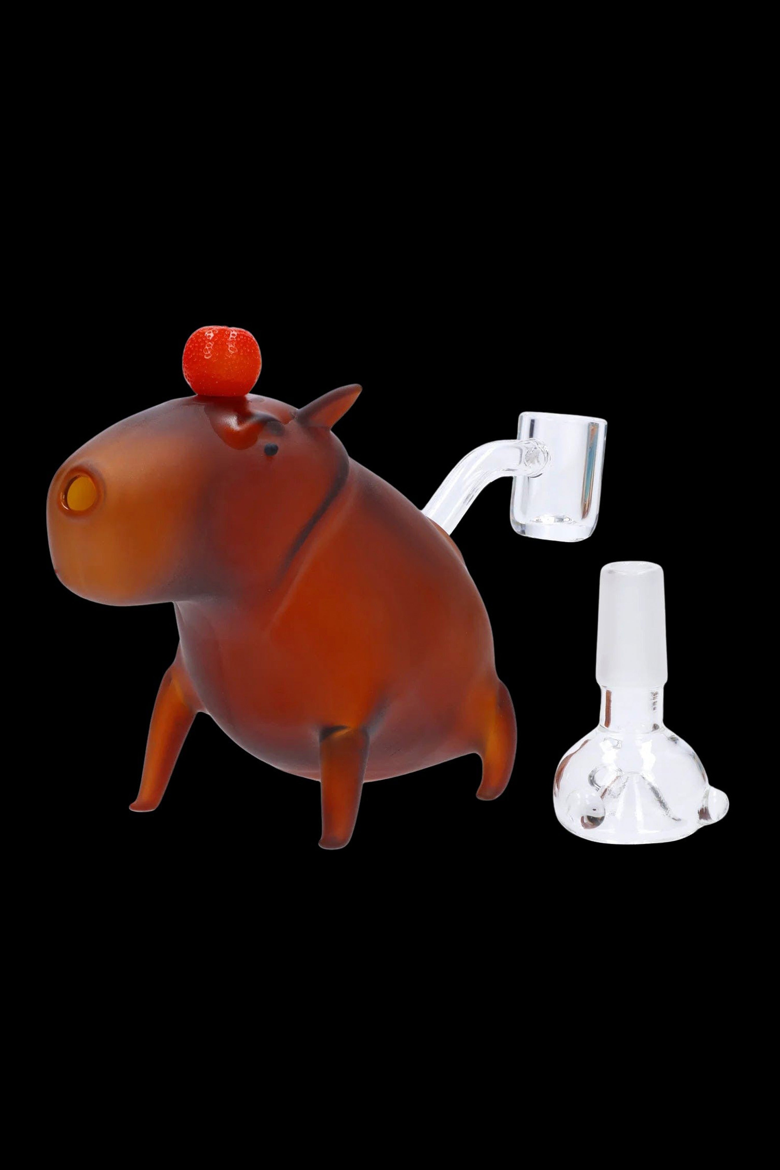 Orange glass hippopotamus sculpture with a clear glass oil rig and dab nail beside it on a black background.