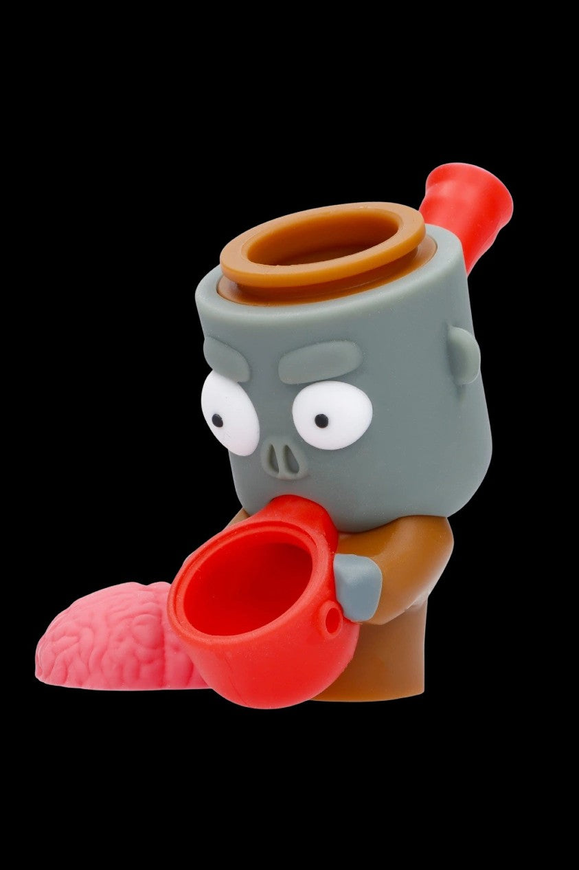 A cartoon zombie-themed glass pipe with a red bowl and brain-shaped accessory, isolated on a black background.