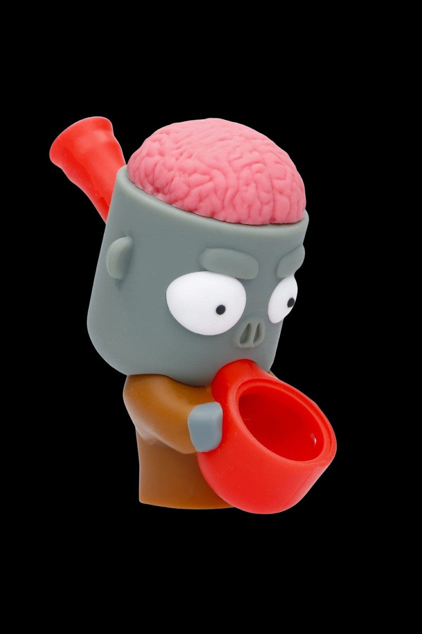 Cartoon zombie-themed glass pipe with a pink brain exposed on top, isolated on a black background.