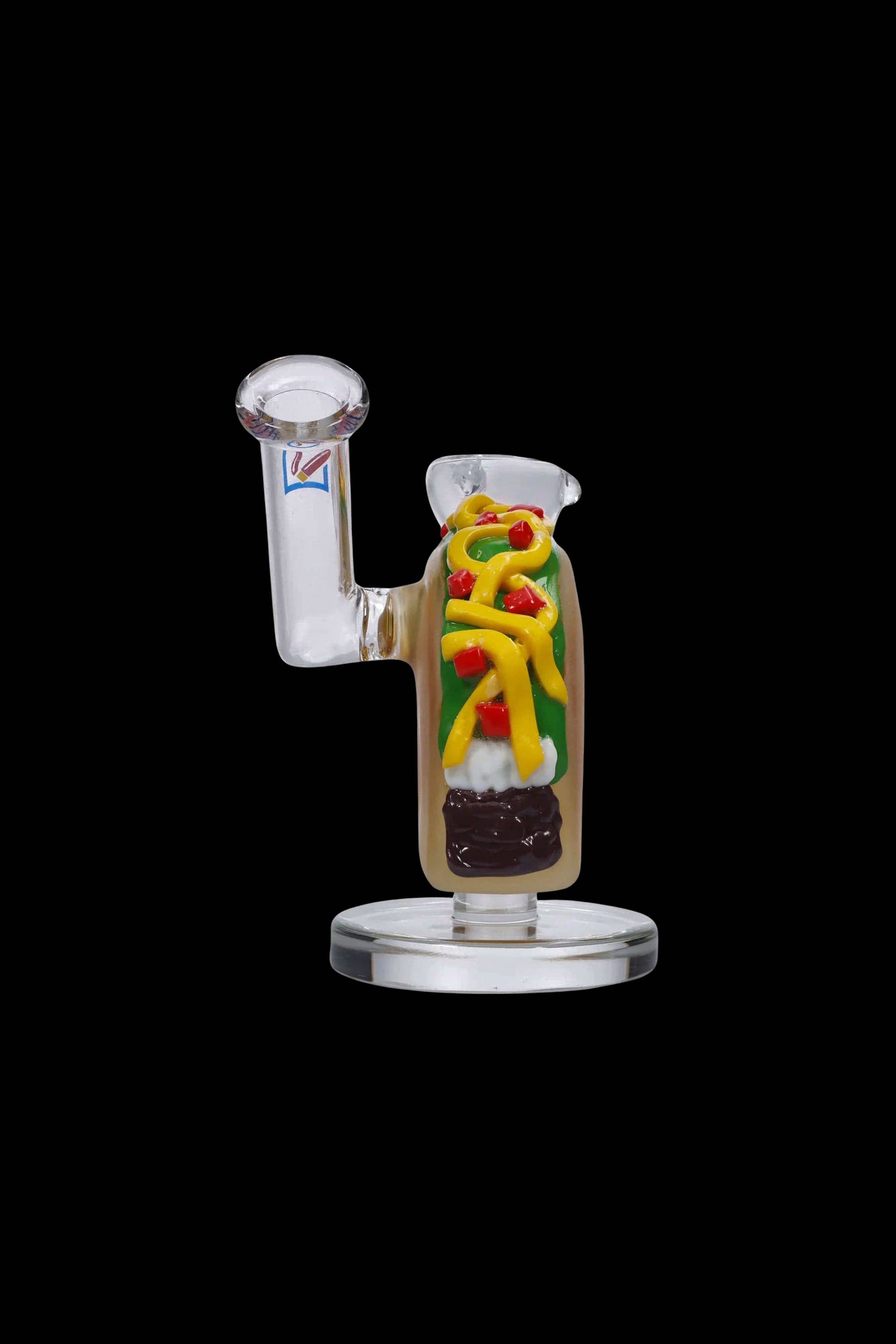 Glass rig shaped like a hot dog with colorful toppings, isolated on a black background.