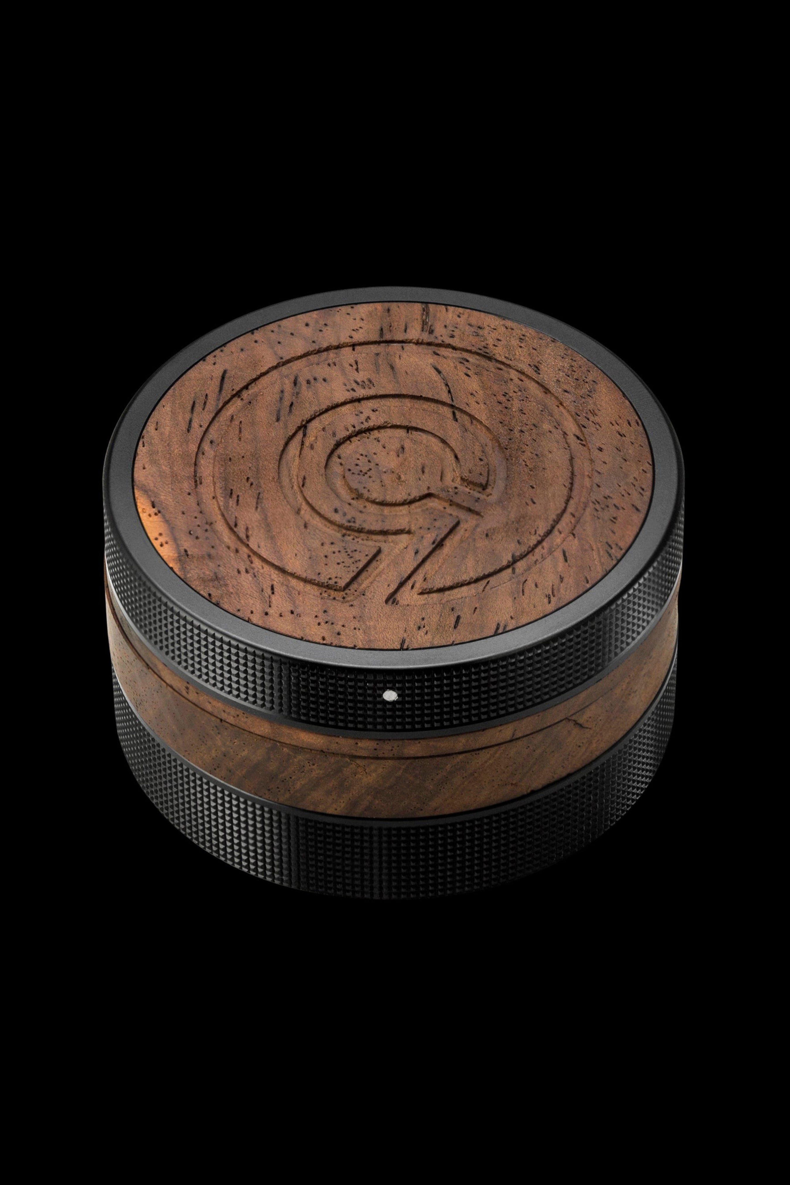 Wood and metal cannabis grinder with engraved logo on a black background.
