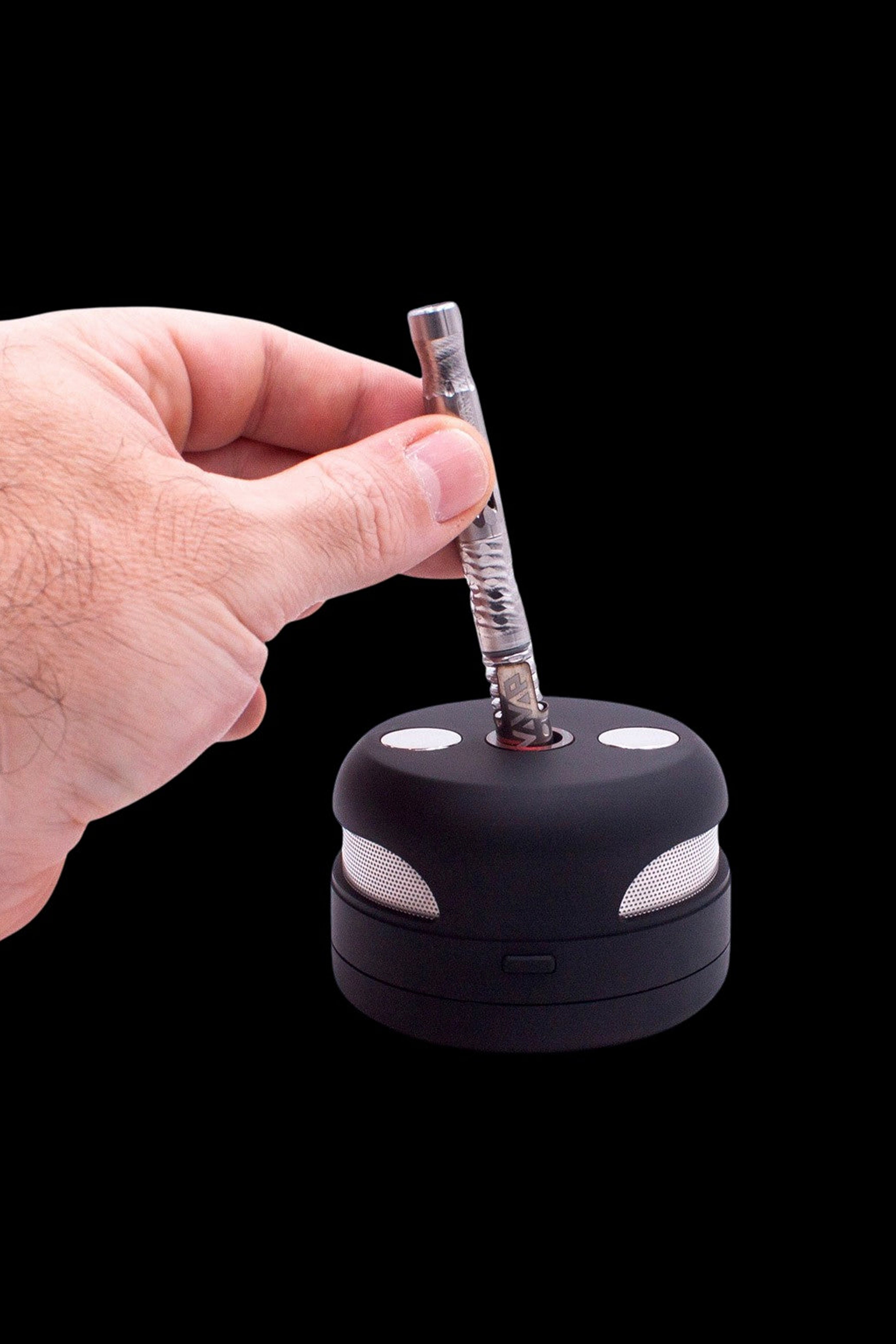 Hand inserting a cannabis oil dab straw into a portable electronic dab rig on a black background.