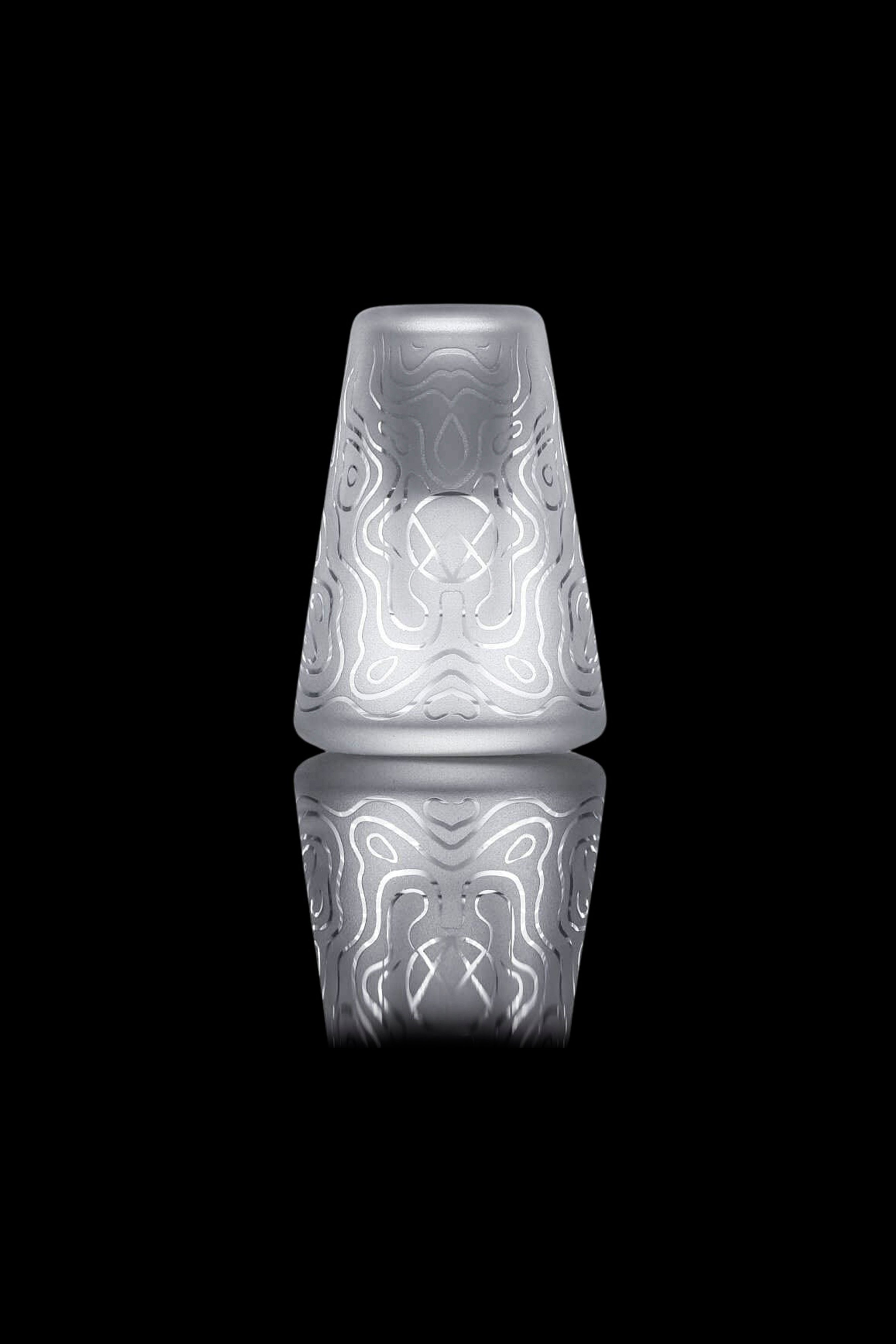 Frosted glass cannabis water pipe with intricate floral carvings, reflected on a dark surface.