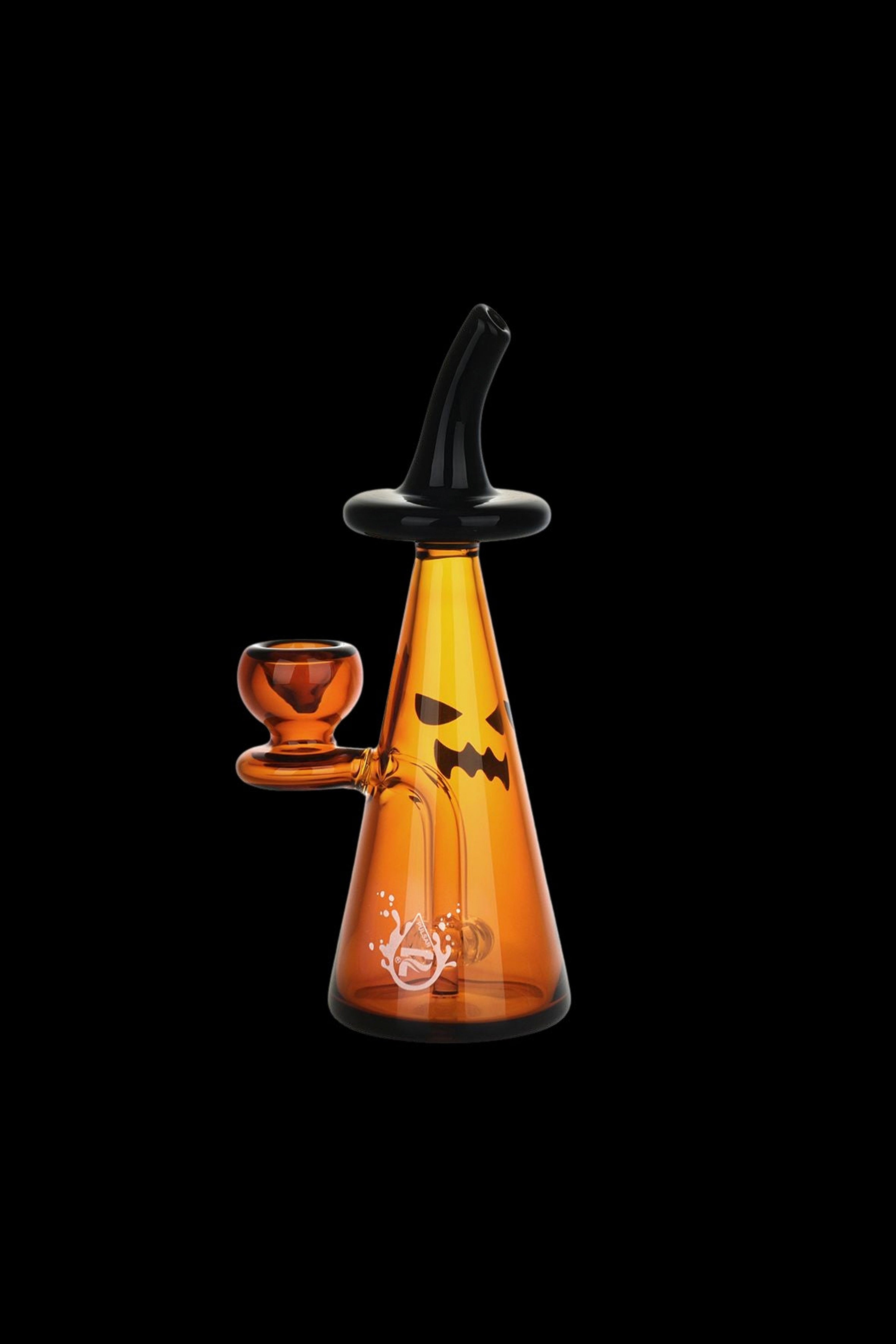 Orange glass water pipe with jack-o'-lantern face and accompanying bowl, isolated on black.