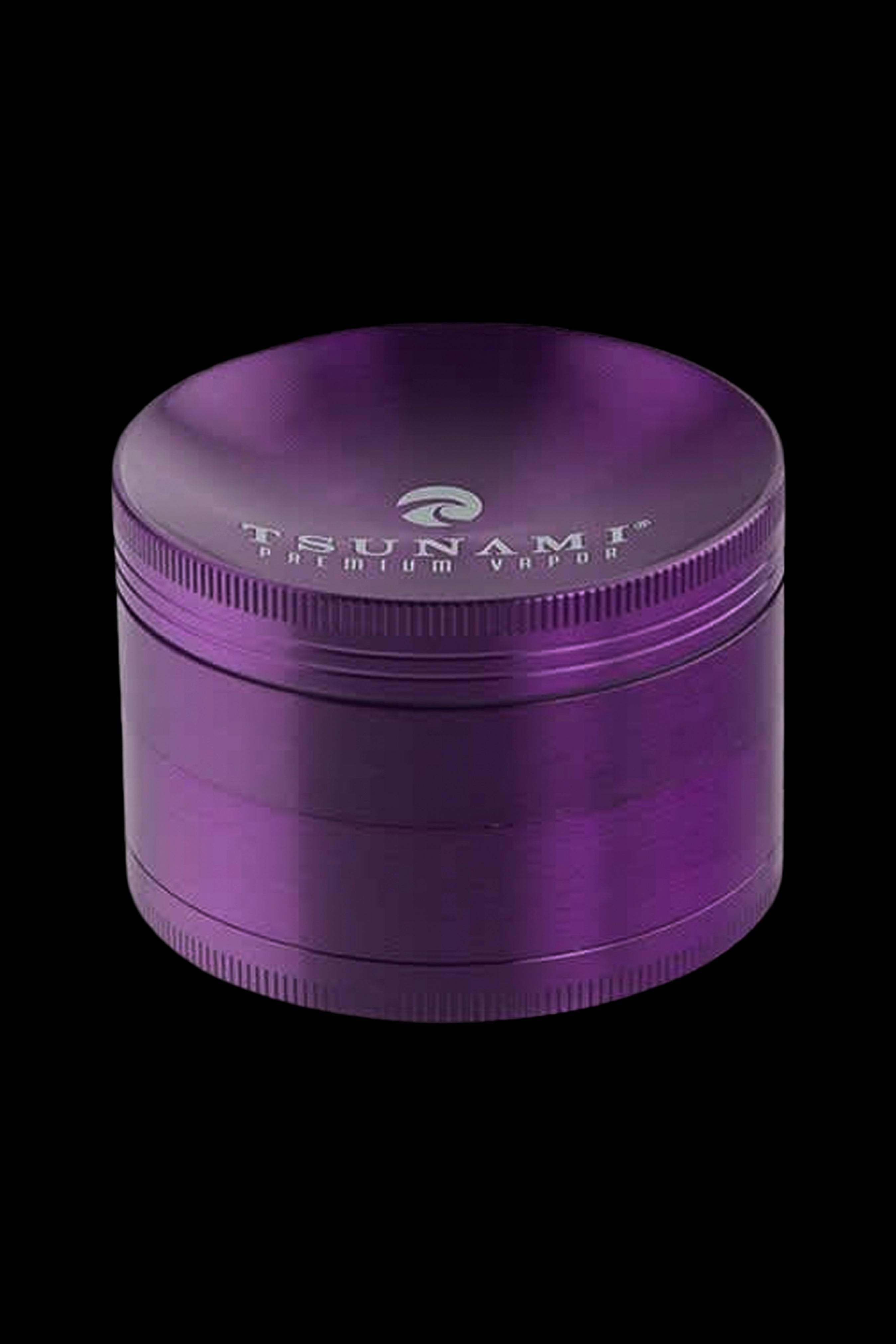 Purple four-piece metal grinder with "TSUNAMI PREMIUM VAPOR" etched around the lid.