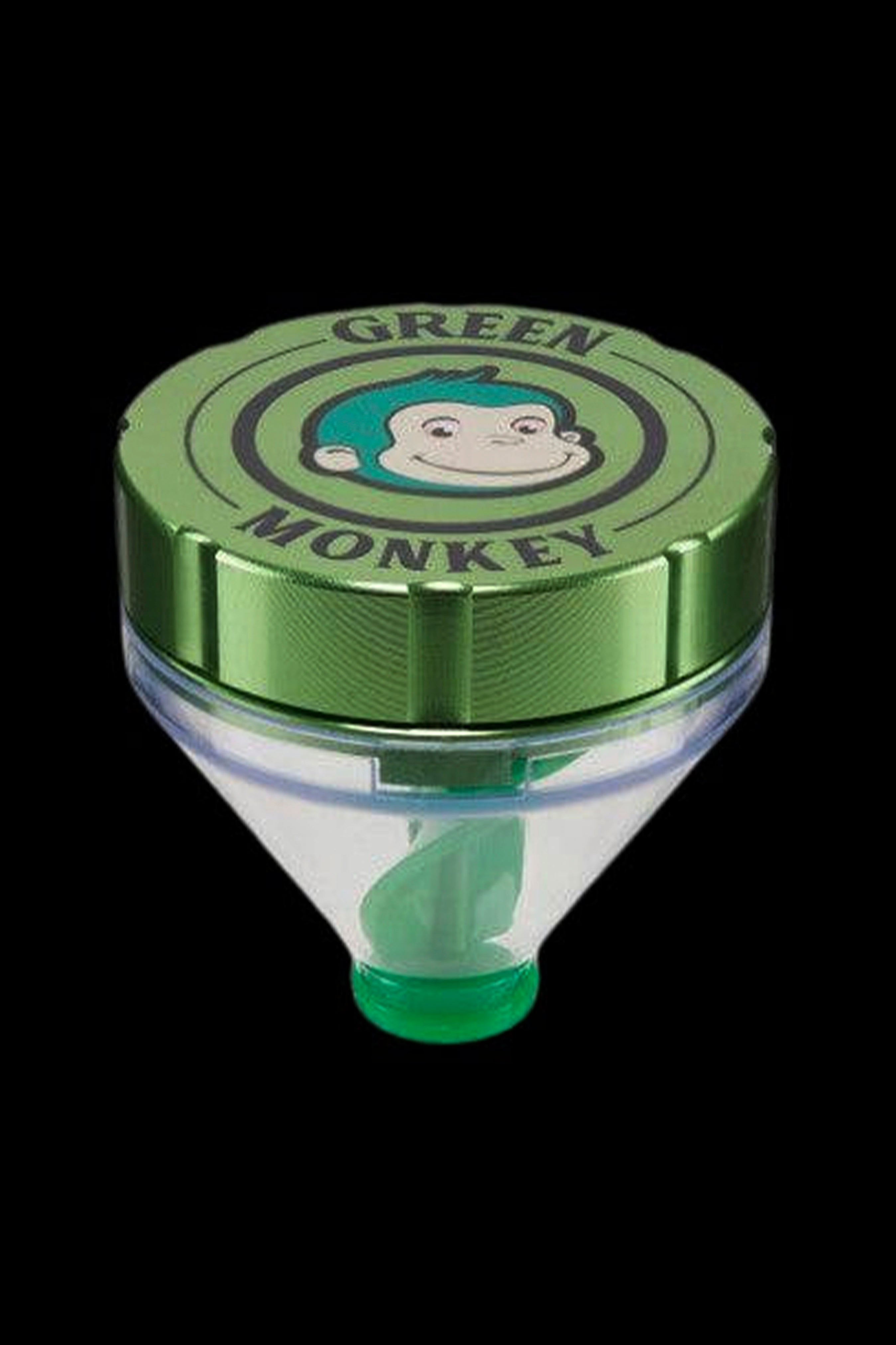 Top-down view of a green metal lid featuring the smiling cartoon logo on the Green Monkey Patas Grinder against a black background.
