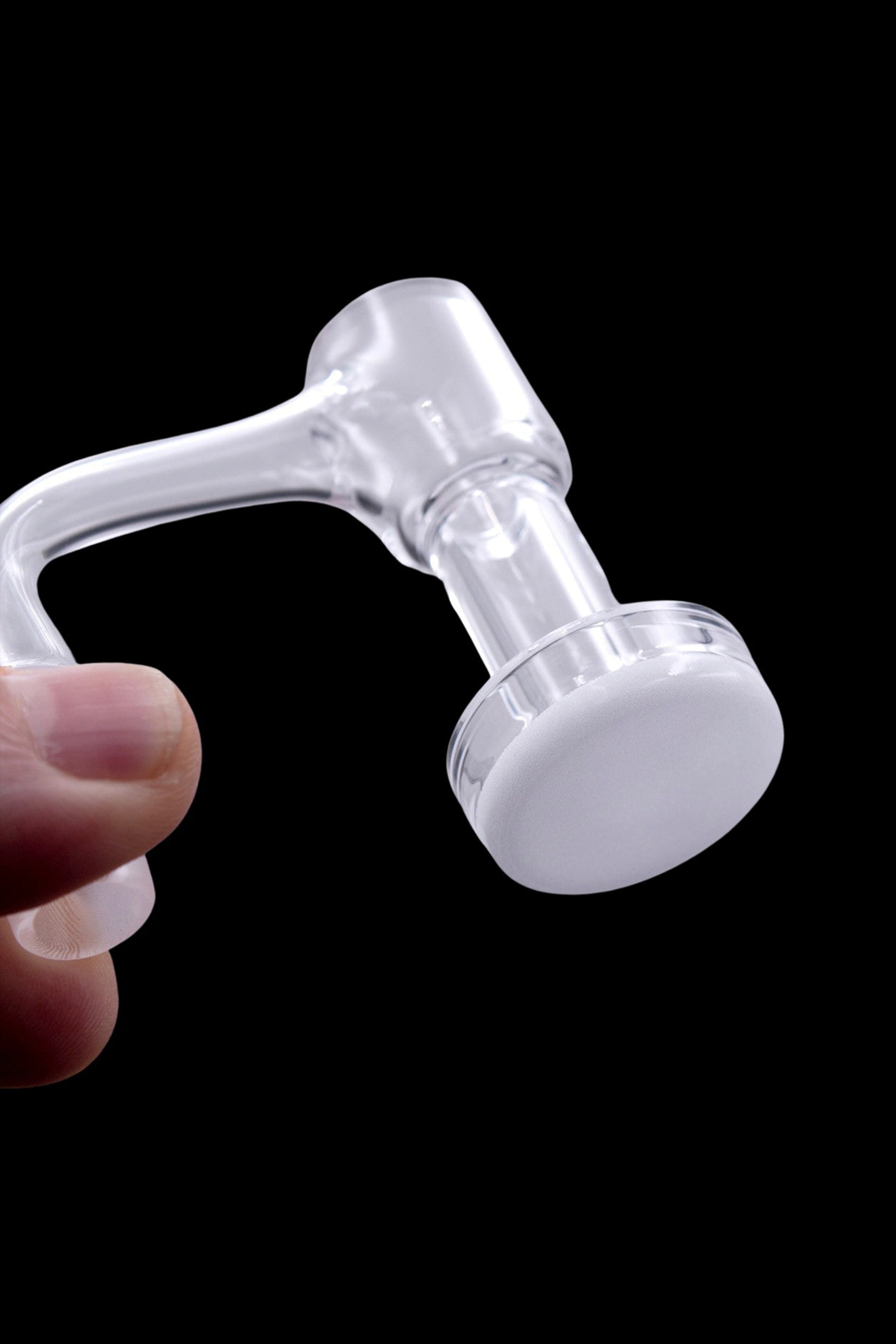 Clear glass oil rig for cannabis concentrate use, held in a hand against a black background.