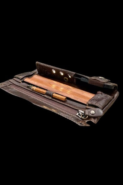 Leather cannabis kit with a joint, papers, and tools inside, displayed open on a black background.