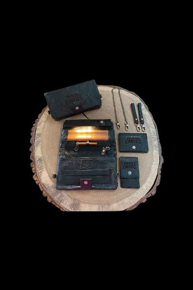 Dark green cannabis accessories—cases, grinder, and tools—arranged on a rustic wooden slice against a black background.