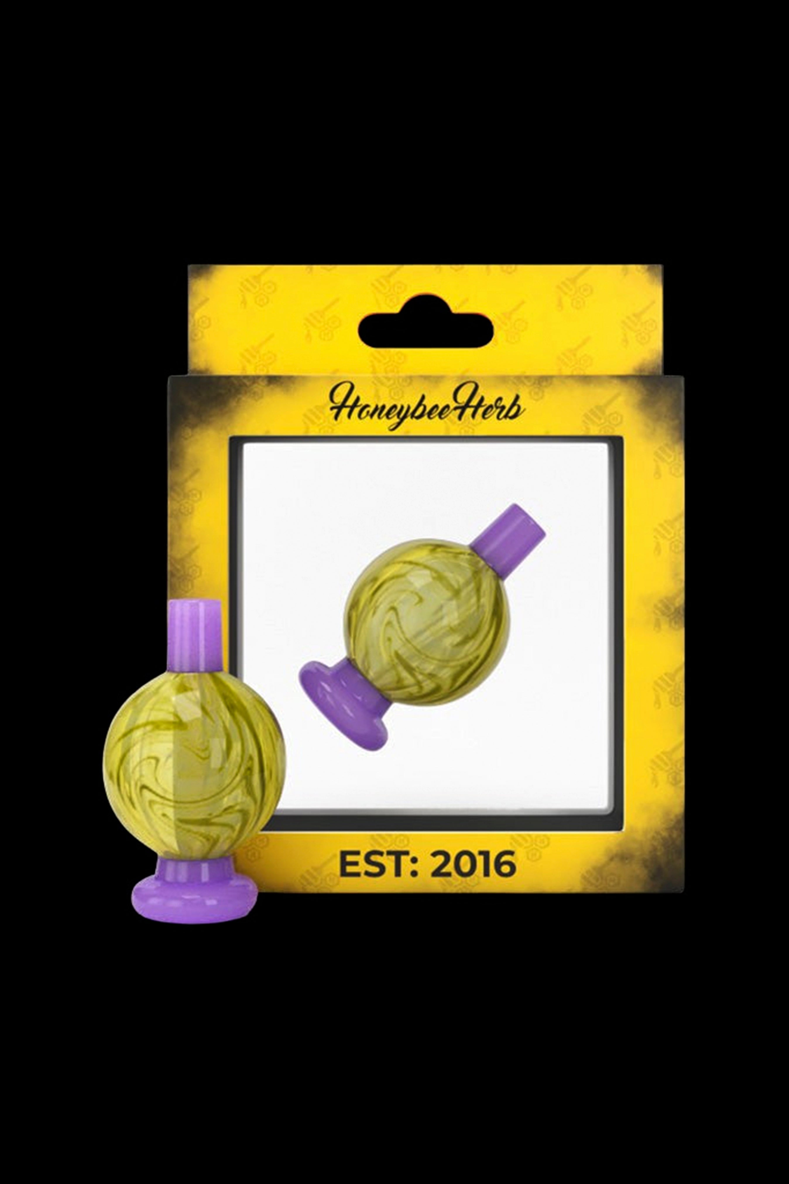 A glass bubbler with a spherical, marbled green and yellow body and a purple stem and mouthpiece, packaged on a yellow card with "Honeybee Herb" logo and "EST. 2016".