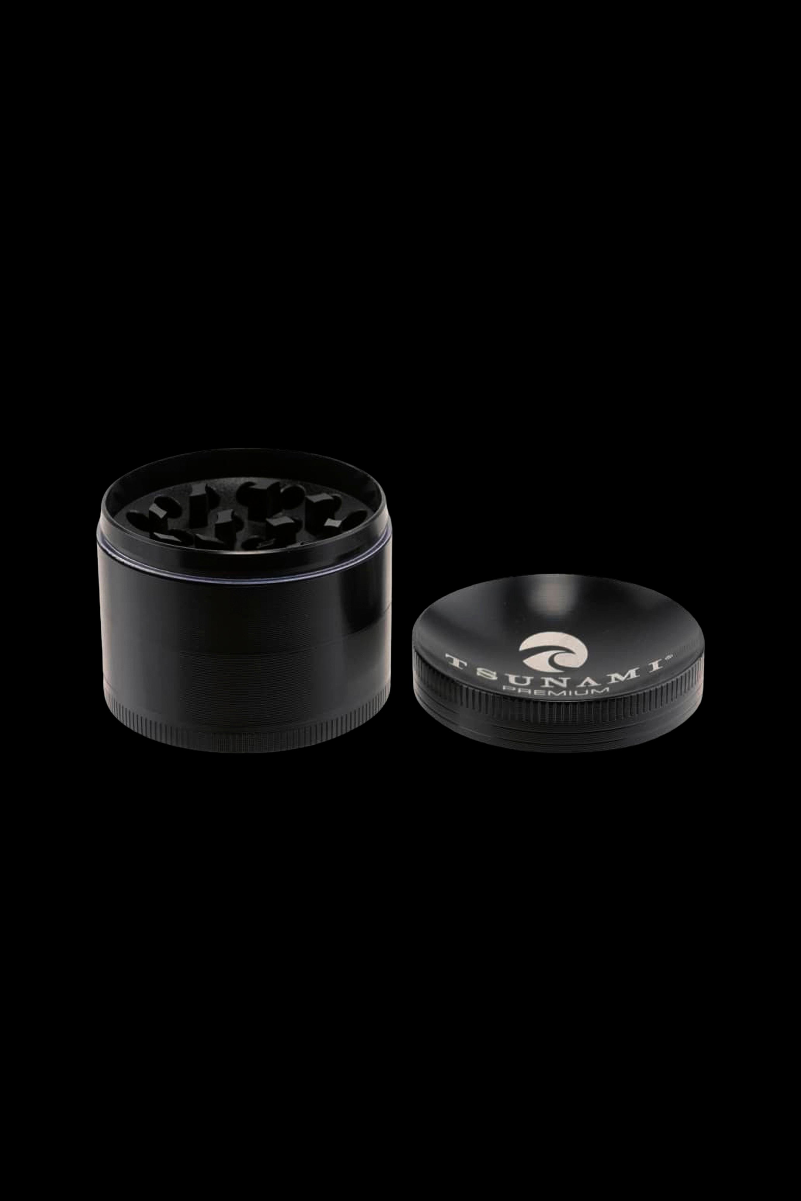 Black four-piece cannabis grinder with metal teeth, open to reveal ground herbs.