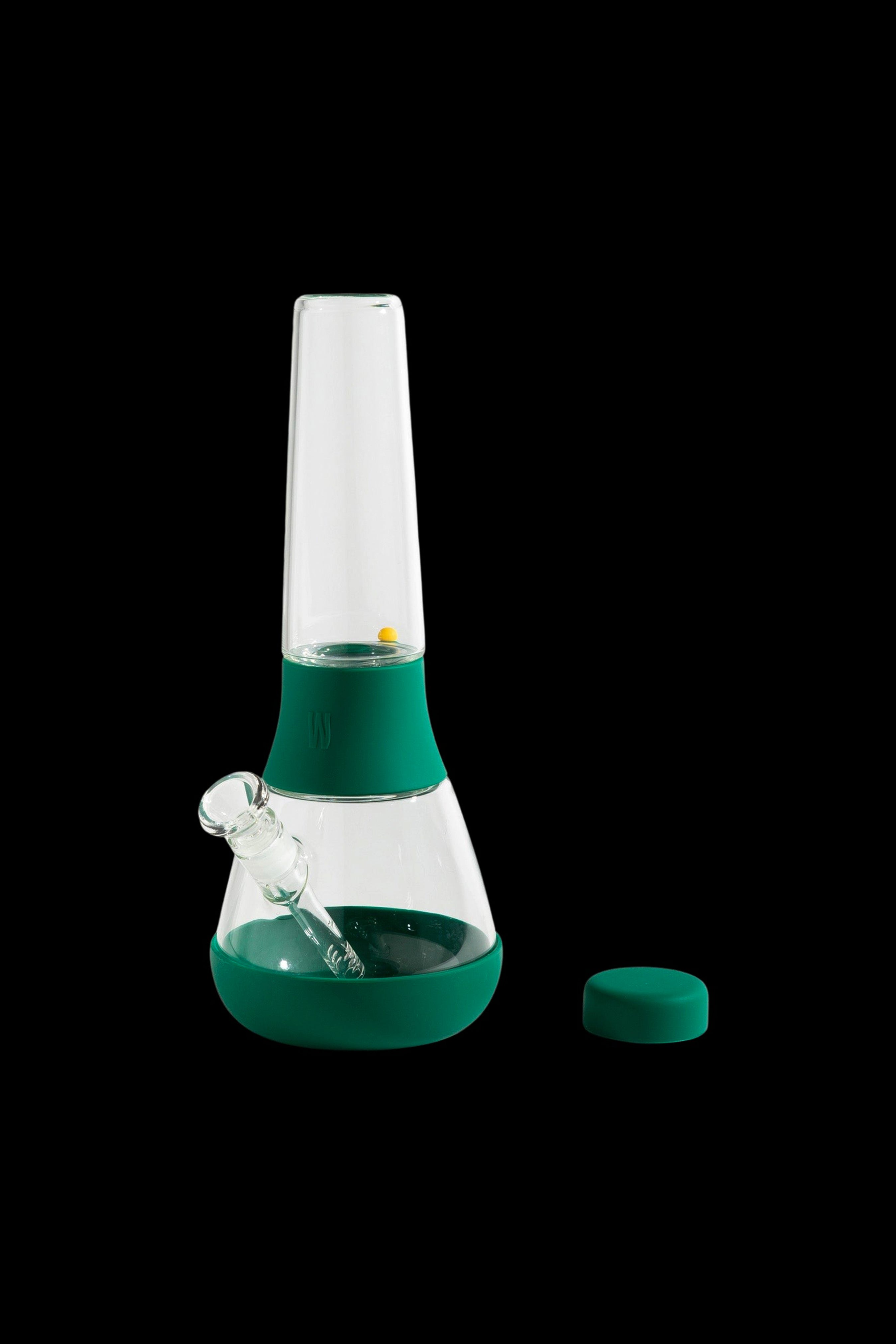 Green silicone bong with a glass downstem and removable lid, isolated on a black background.