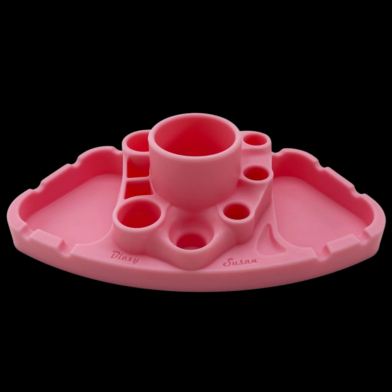 Low-angle front view of the pink Blazy Susan Deluxe Dab Station showing its central cup, multiple surrounding wells, and scalloped edge against a black background.