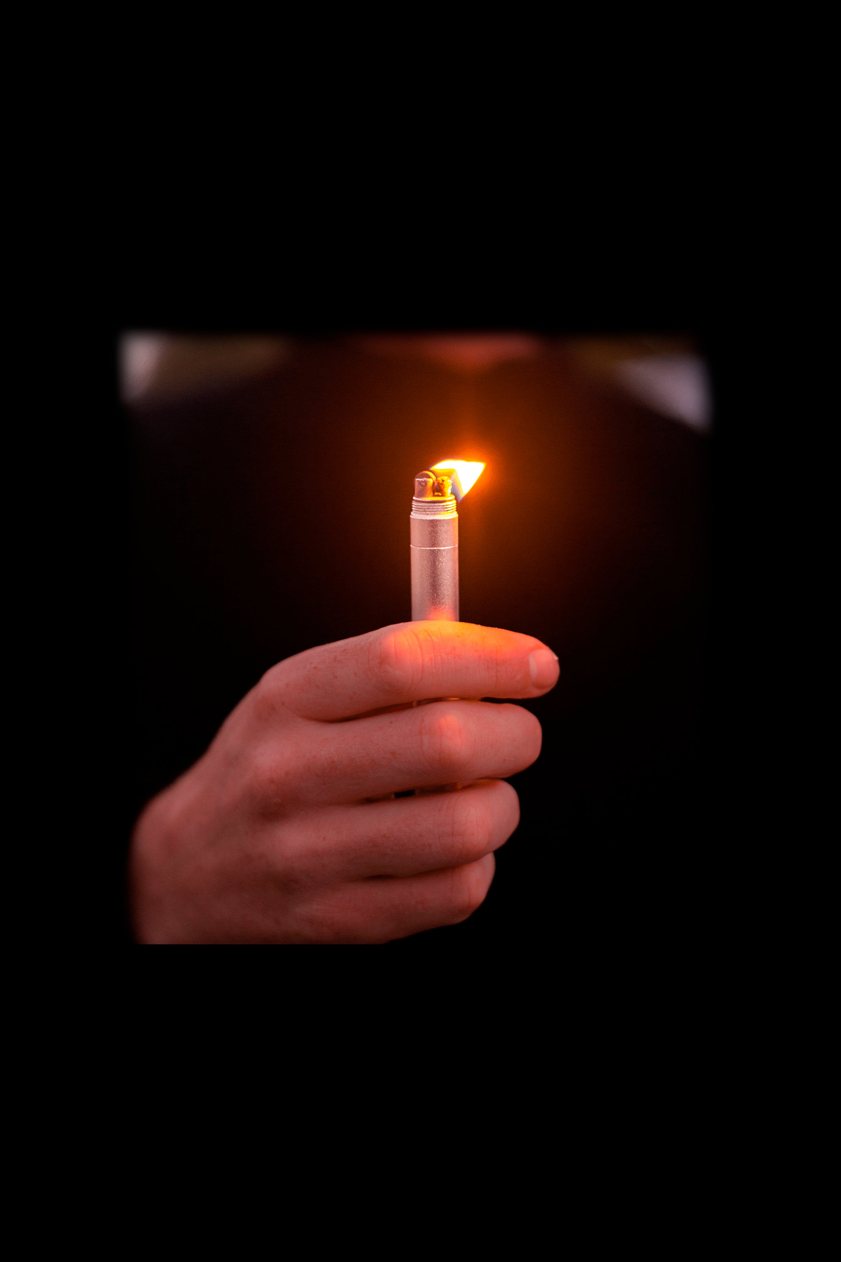 Hand holding a lit lighter in the dark.