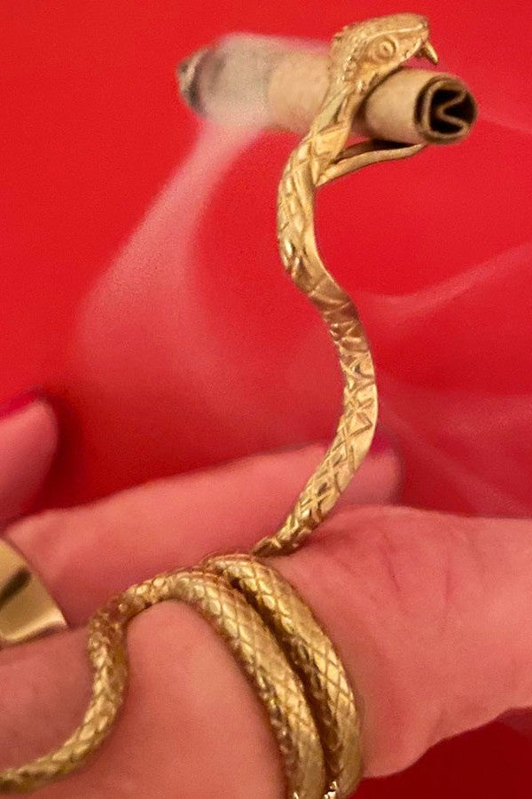 Golden snake-shaped smoking accessory holding a rolled cannabis joint.