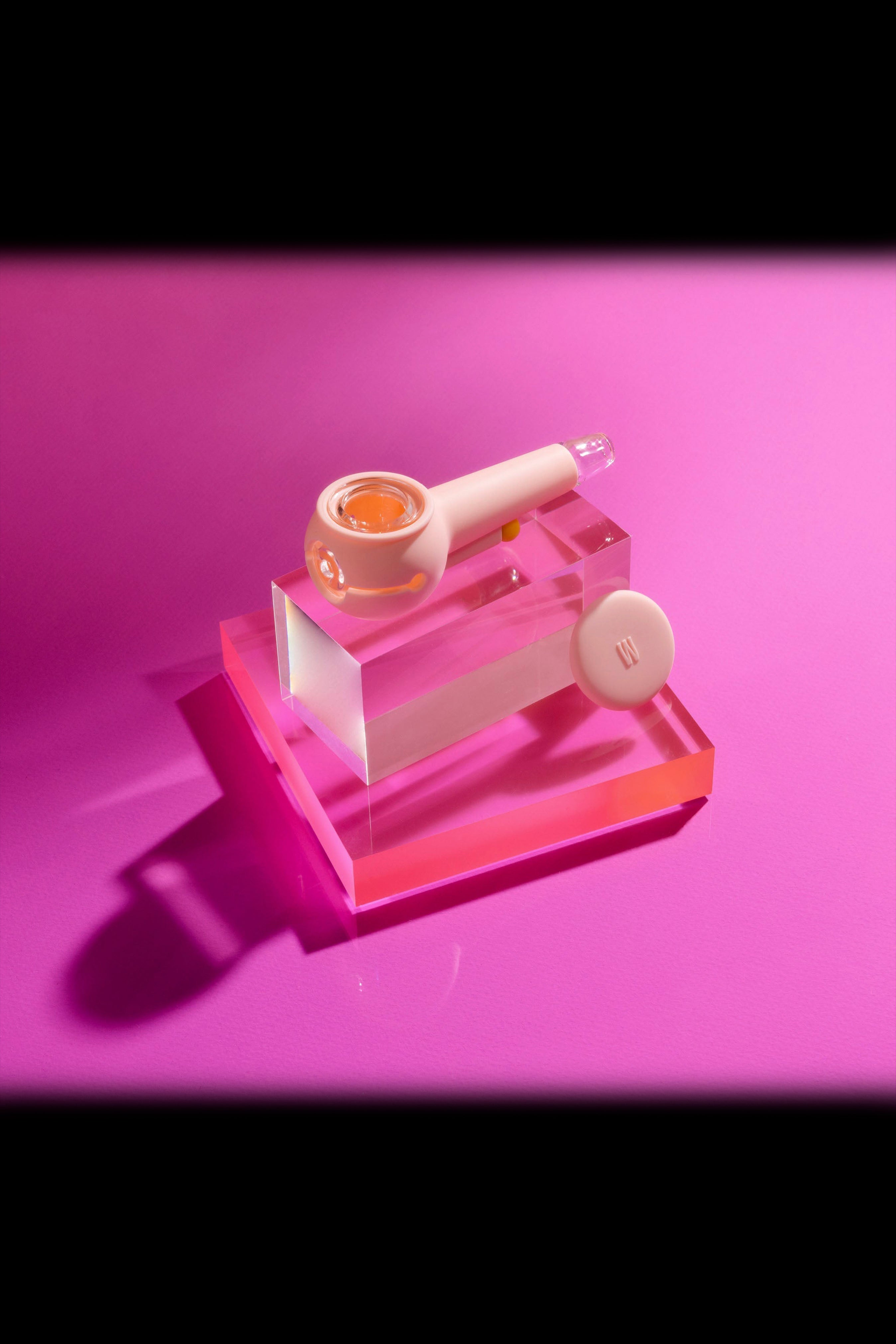 Pink glass cannabis pipe and concentrate on acrylic display, illuminated with pink light.