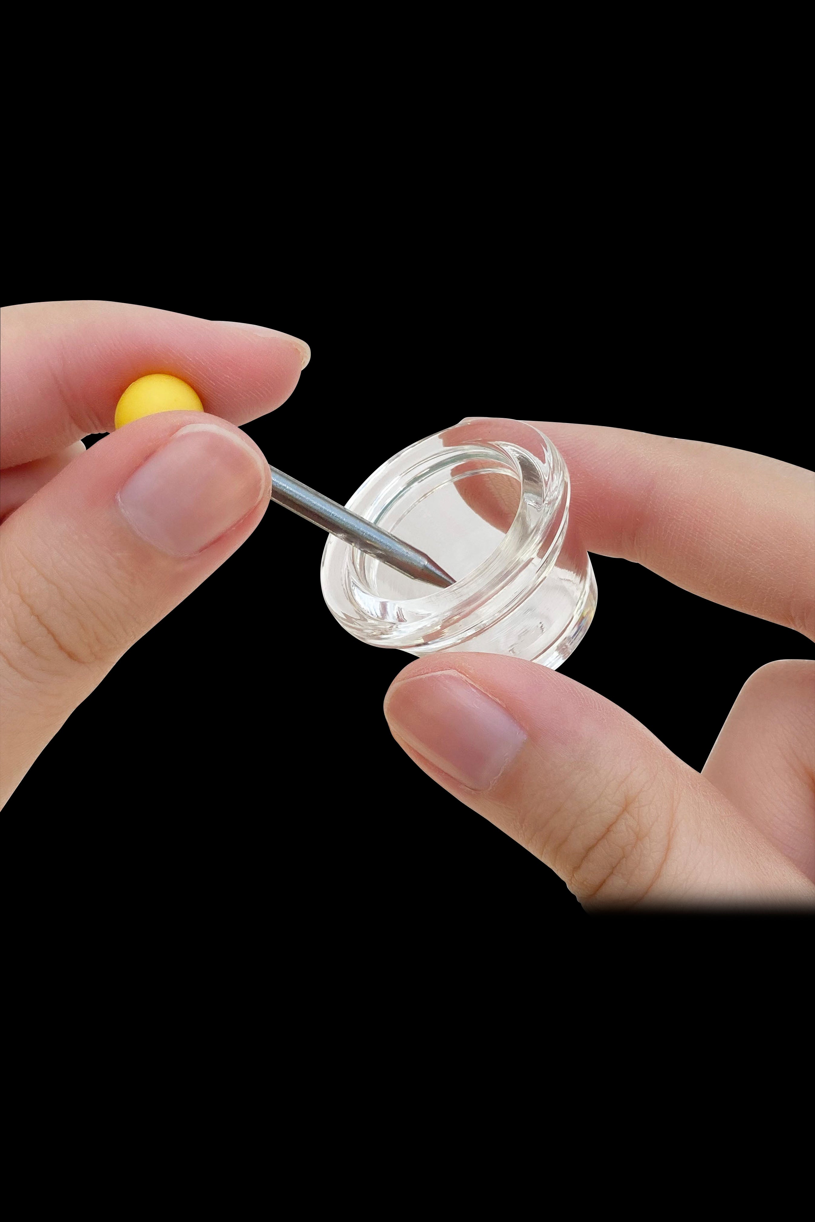 Hand applying a dab tool to a clear quartz banger.