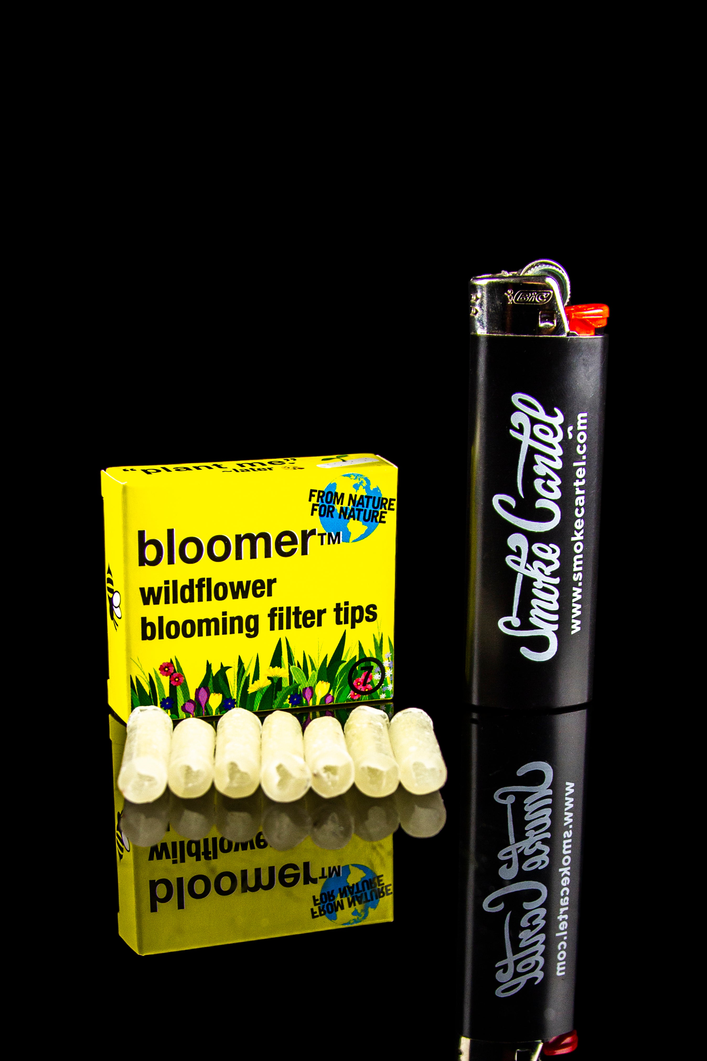 Box of Bloomer wildflower blooming filter tips beside a black Smoke Cartel lighter on a dark background.