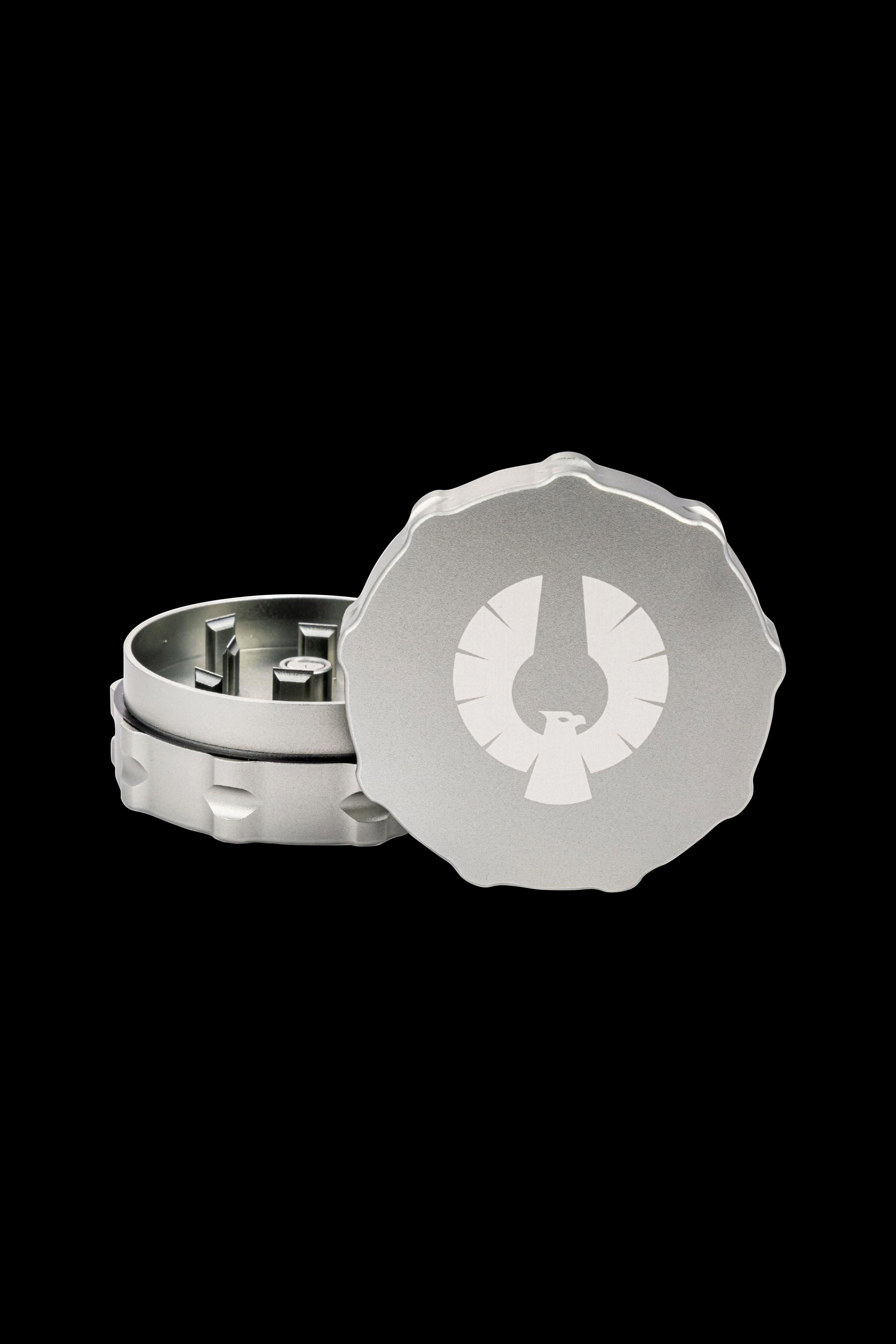 Silver cannabis grinder with a circular design featuring a stylized leaf emblem, open to reveal the internal grinding components.