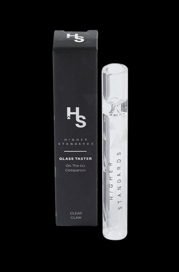 Product-style front view of the Higher Standards Glass Taster: a clear glass tube standing beside its black branded box on a black background