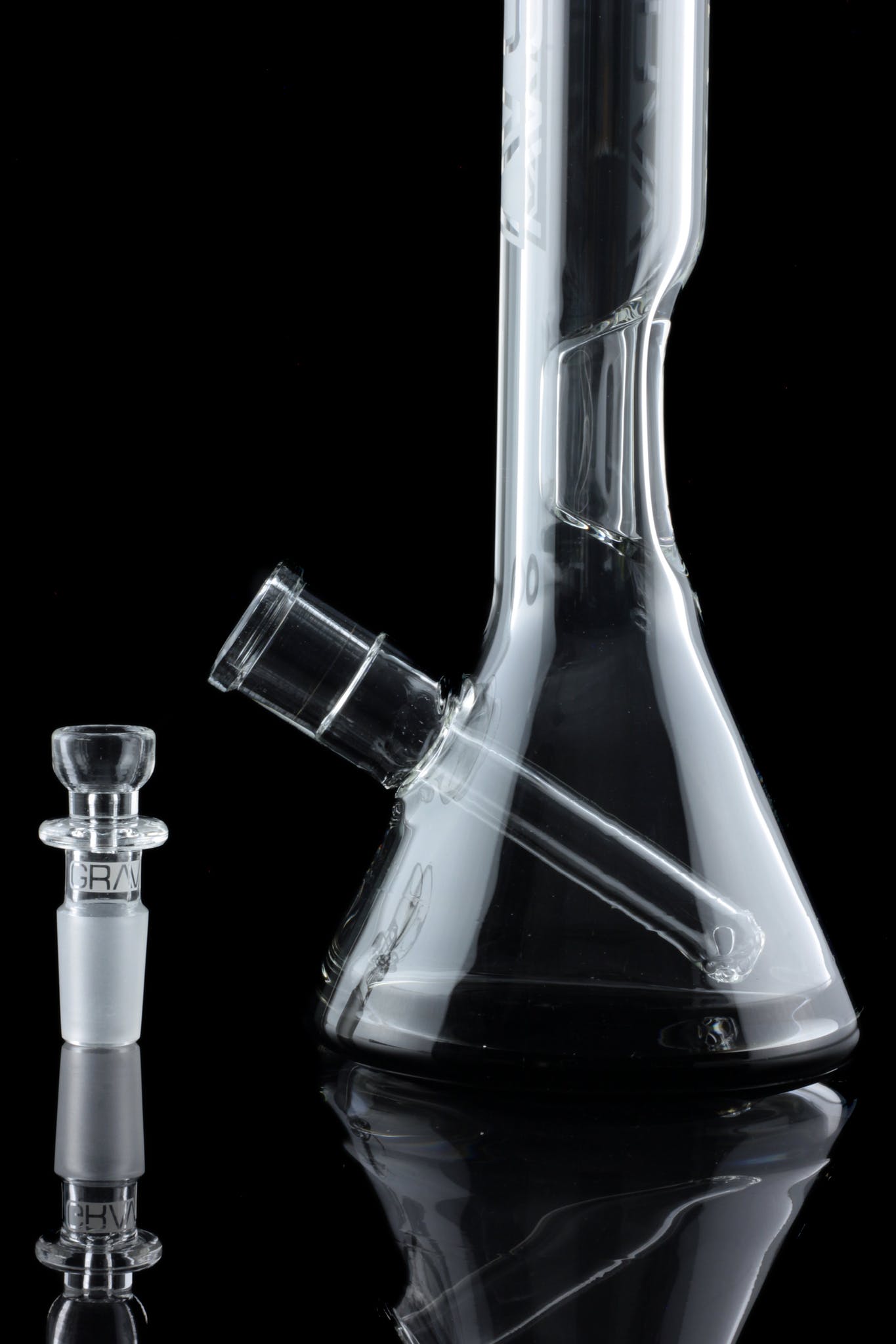 Clear glass water pipe (bong) and detachable downstem, reflected on a black surface.