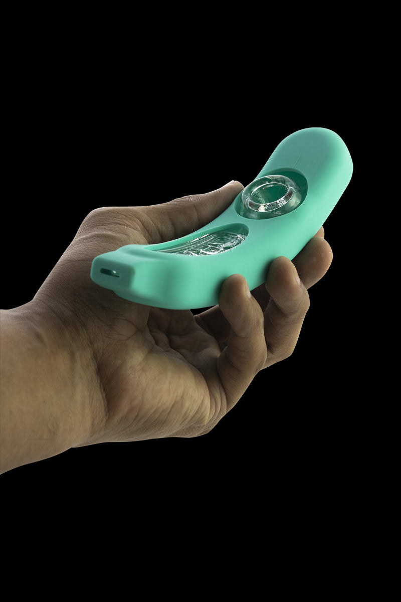 Hand-held perspective of a mint-green GRAV® Rocker Steamroller with Silicone Skin showing the curved body and clear glass bowl against a black background.