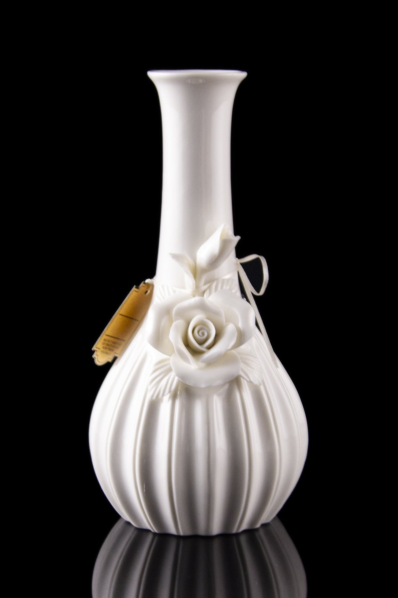 White ceramic bubbler with sculpted roses, reflecting on a black surface.