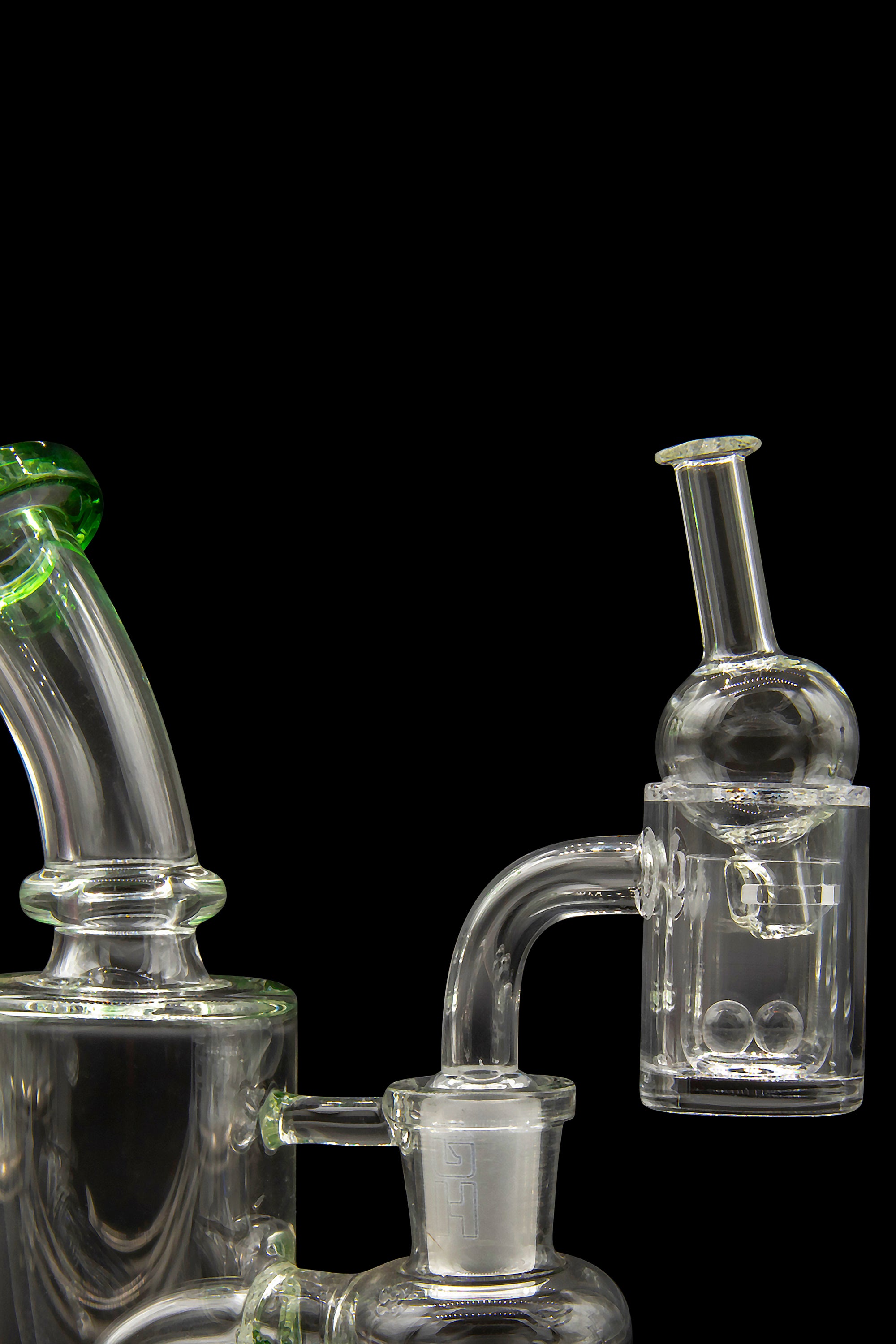 Clear glass cannabis water pipes and dab rig with green accents, isolated on a black background.
