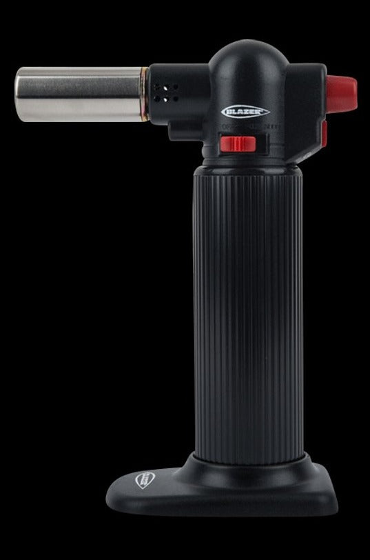 Straight-on studio shot of the Blazer Big Buddy Turbo Torch in black, showing its ribbed cylindrical handle, metal nozzle, red ignition controls and flat base.