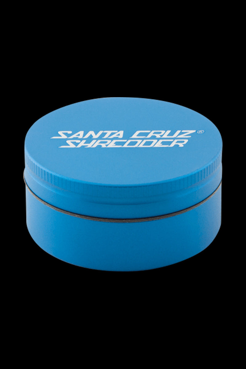 Top-down view of a small blue Santa Cruz Shredder 2-Piece Grinder with white logo on the lid against a black background