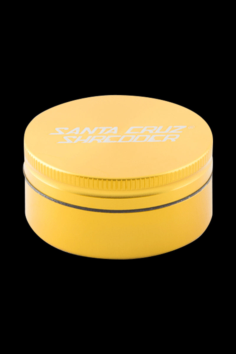 Top-down oblique view of a gold Santa Cruz Shredder 2-Piece Grinder centered on a black background, showing the textured lid edge and white logo.