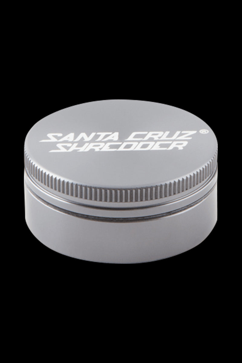 Close-up front view of a matte black Santa Cruz Shredder 2-Piece Grinder centered on a black background, showing the knurled edge and white logo on top.