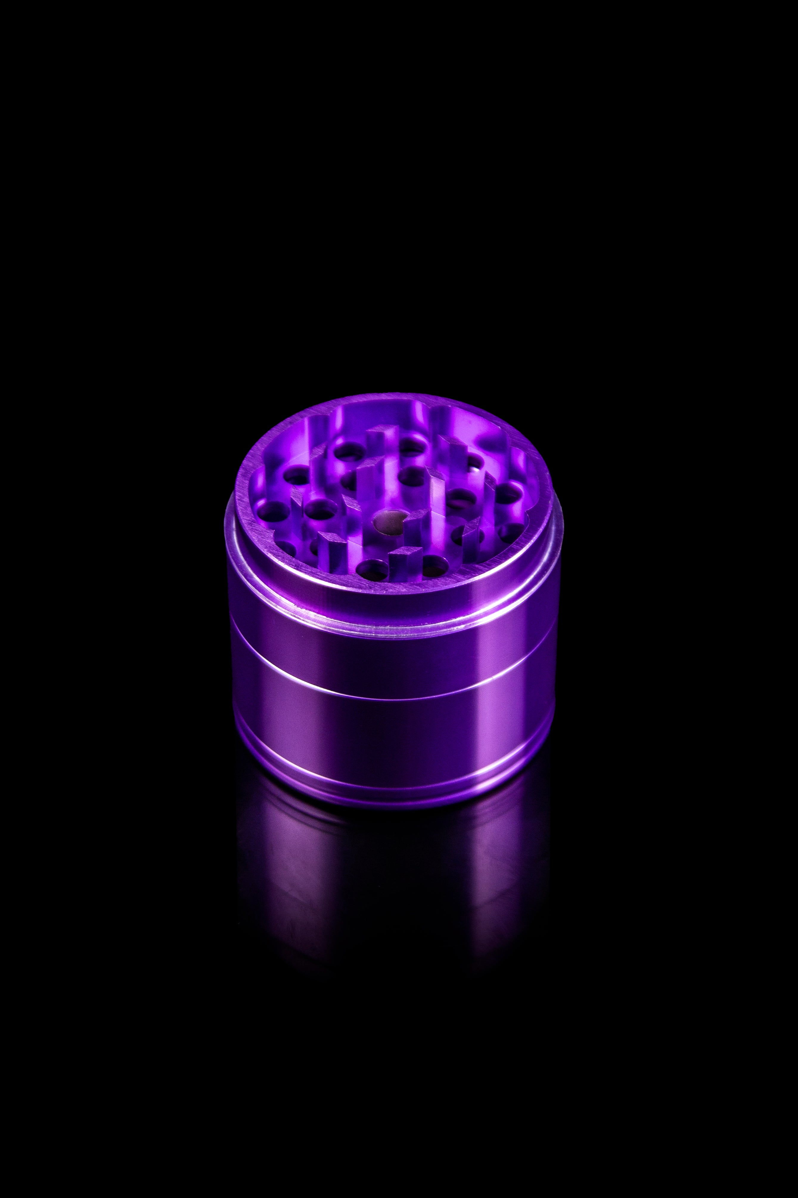 Purple four-piece cannabis grinder on a reflective black surface.