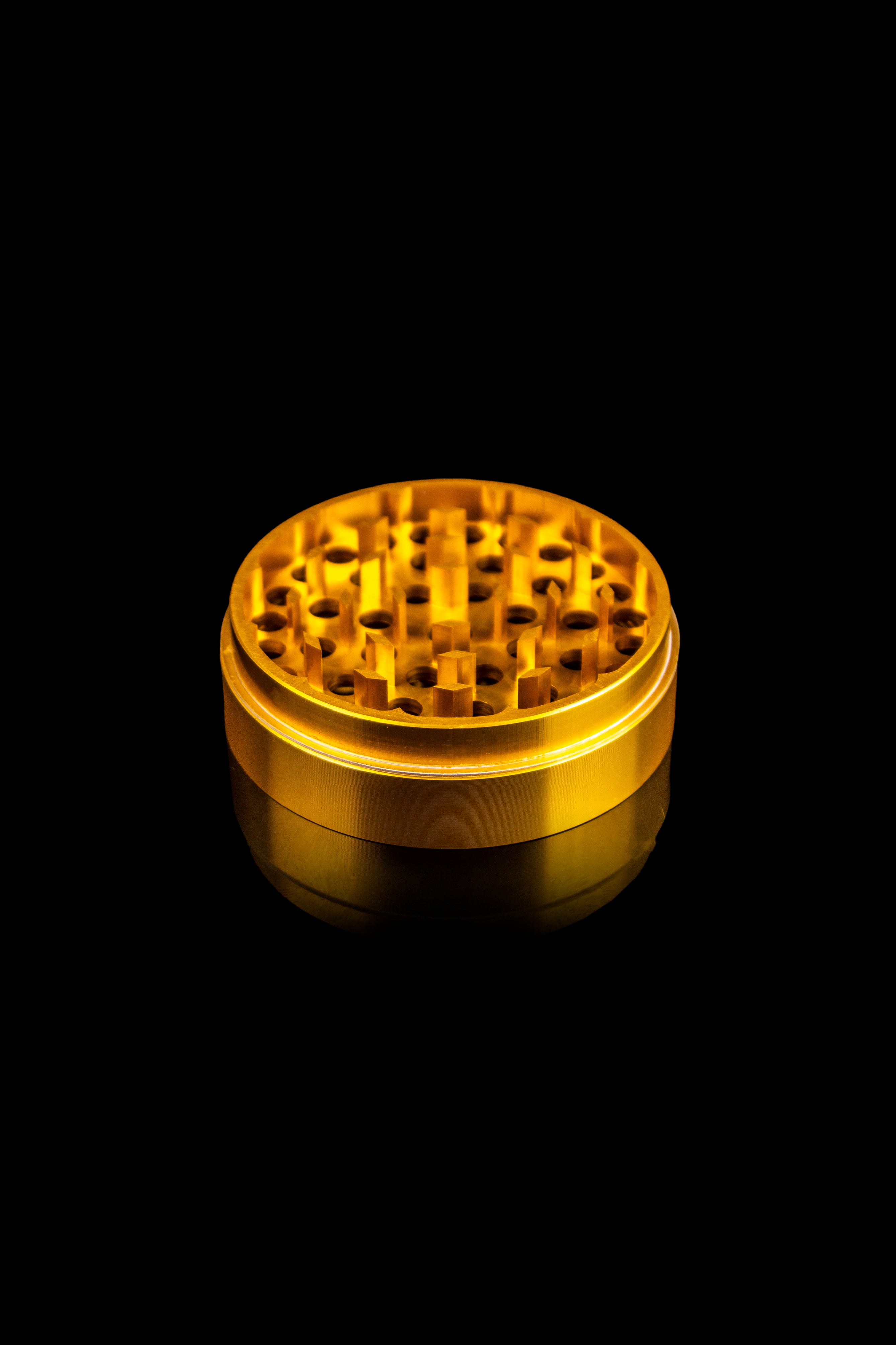Gold cannabis grinder against a black background.